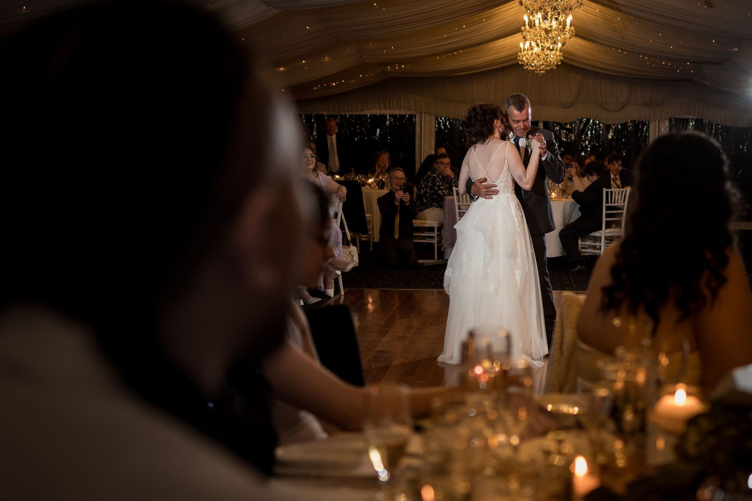 Romantic first dance at wedding reception with candlelit tables in foreground.