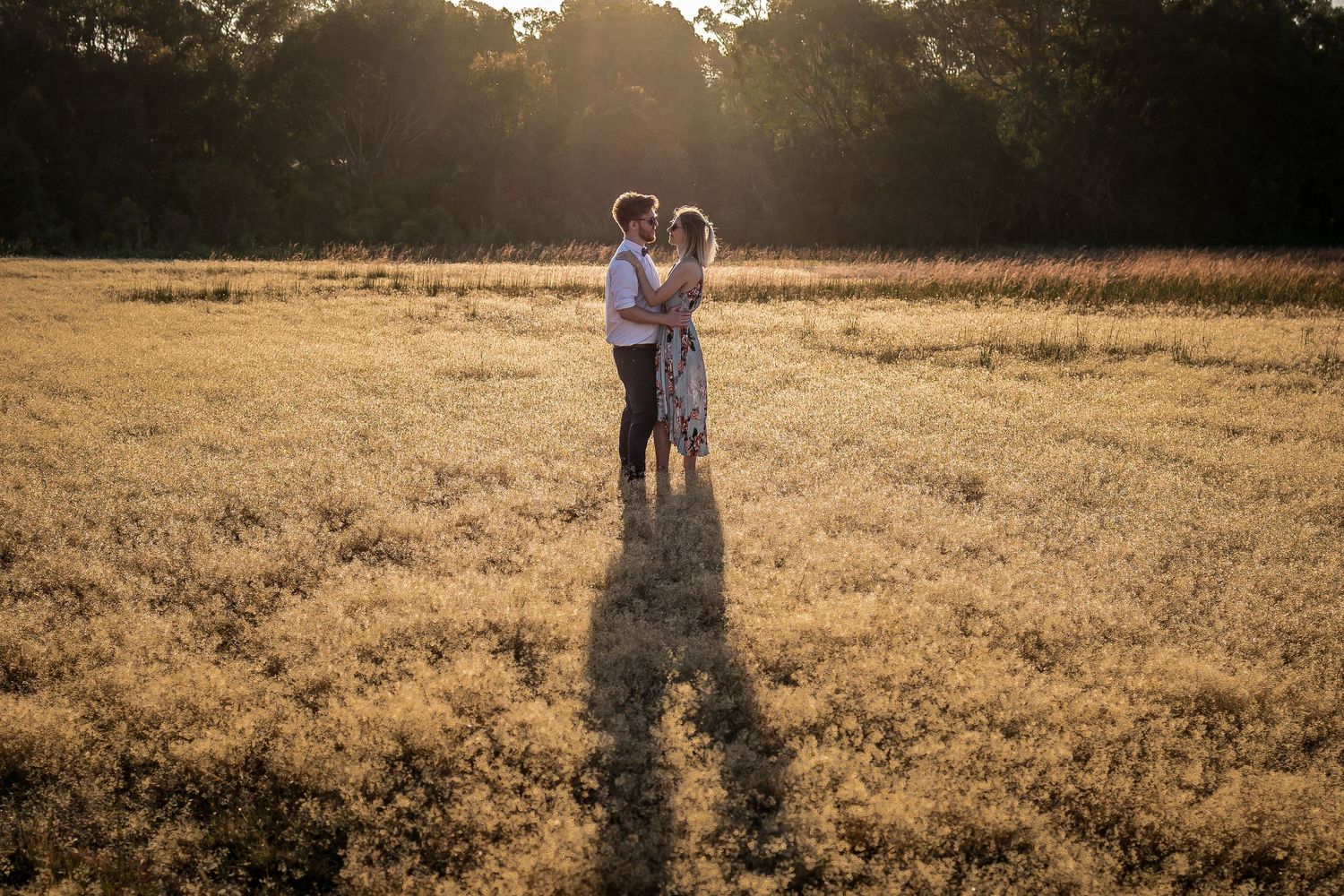 Silhouetted couple standing in golden sunset light in an open field.