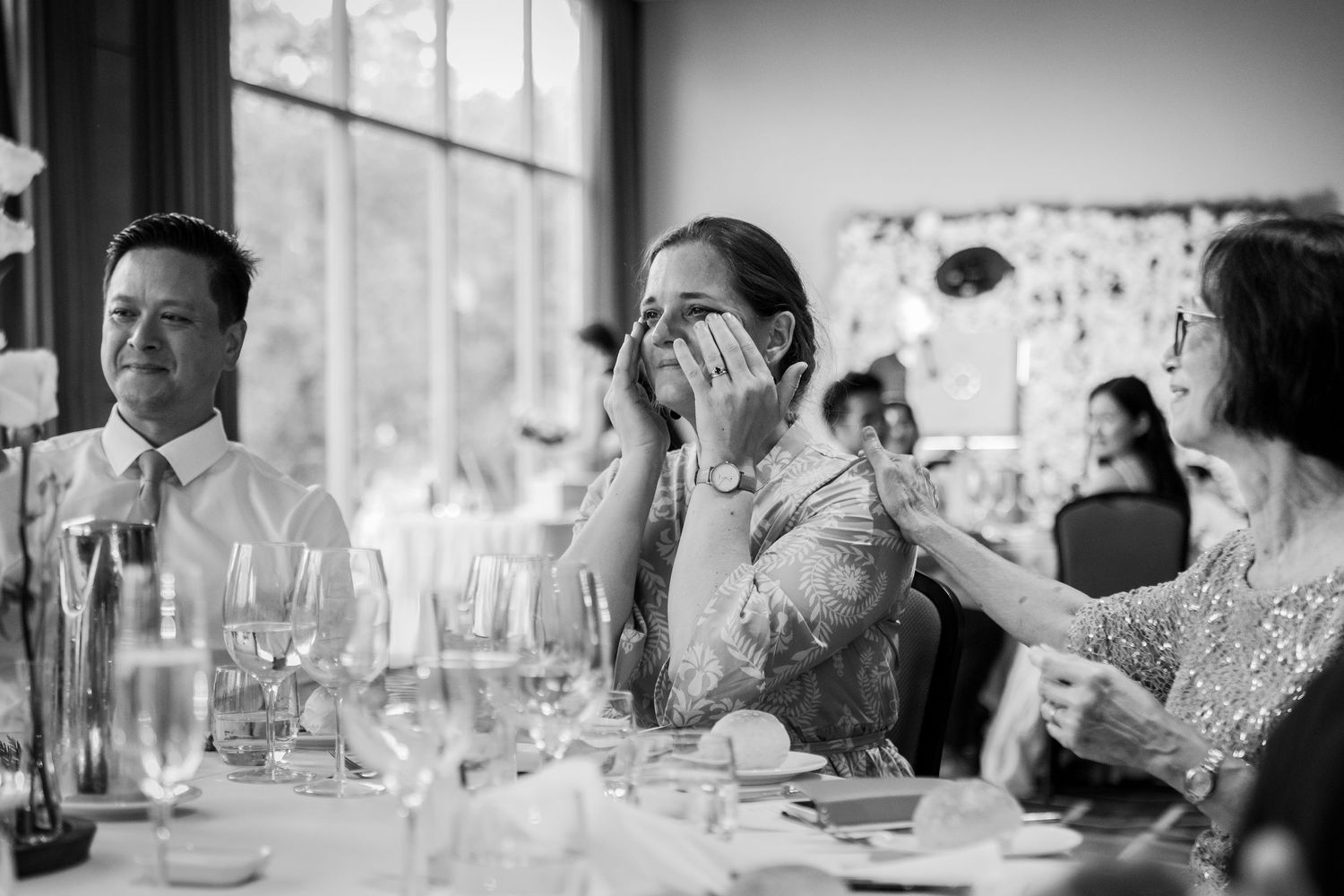 Emotional wedding guest wiping tears during reception speeches at elegant venue.