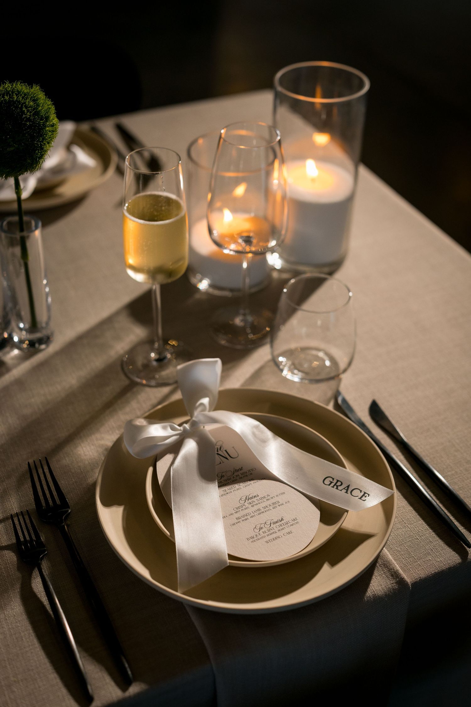 Elegant candlelit wedding table setting with a personalized name card, ribbon-tied menu, champagne glass, and glowing candles.