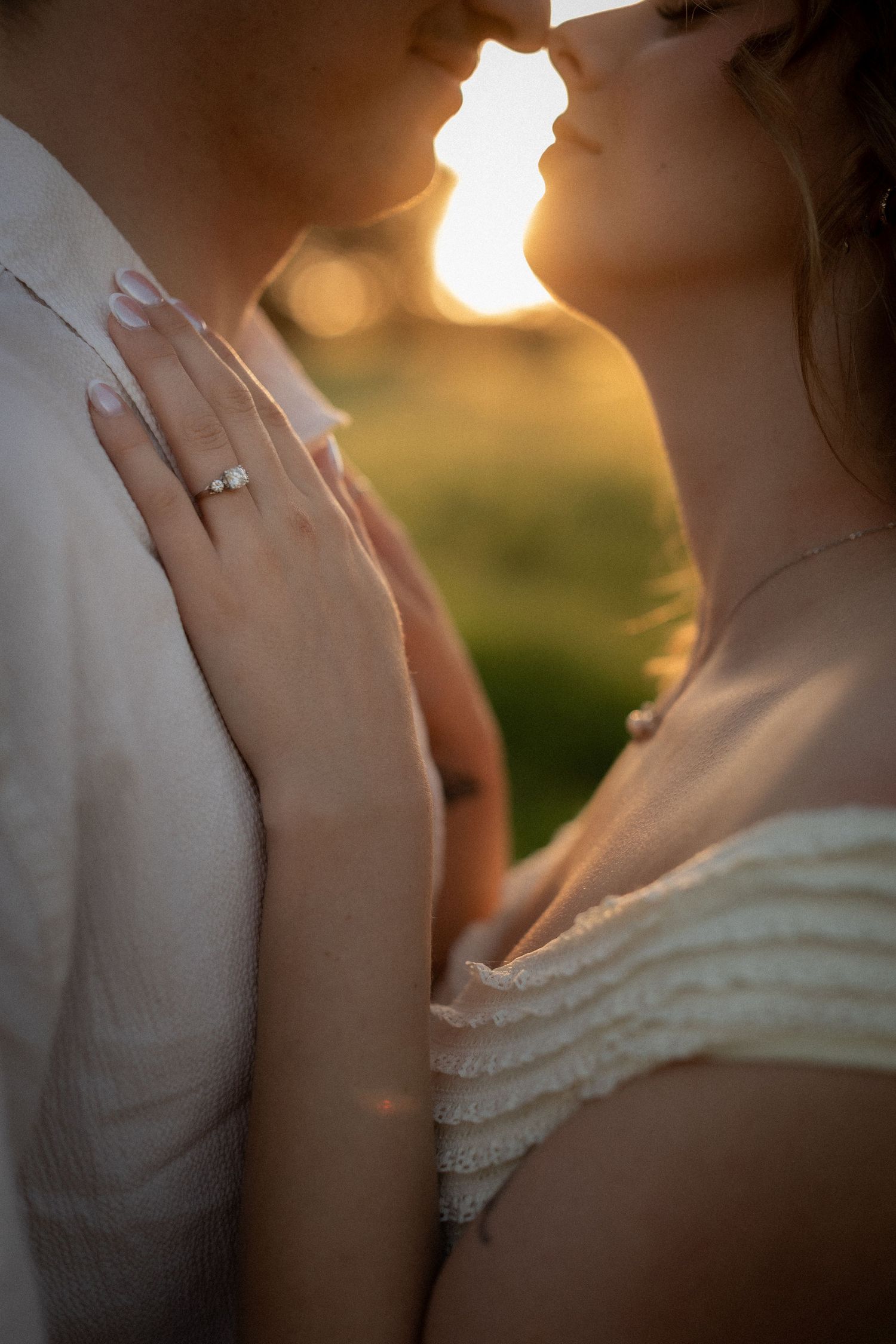 Couple sharing a romantic golden hour moment, woman wearing an engagement ring and white dress, backlit by warm sunset light. at Guildford,