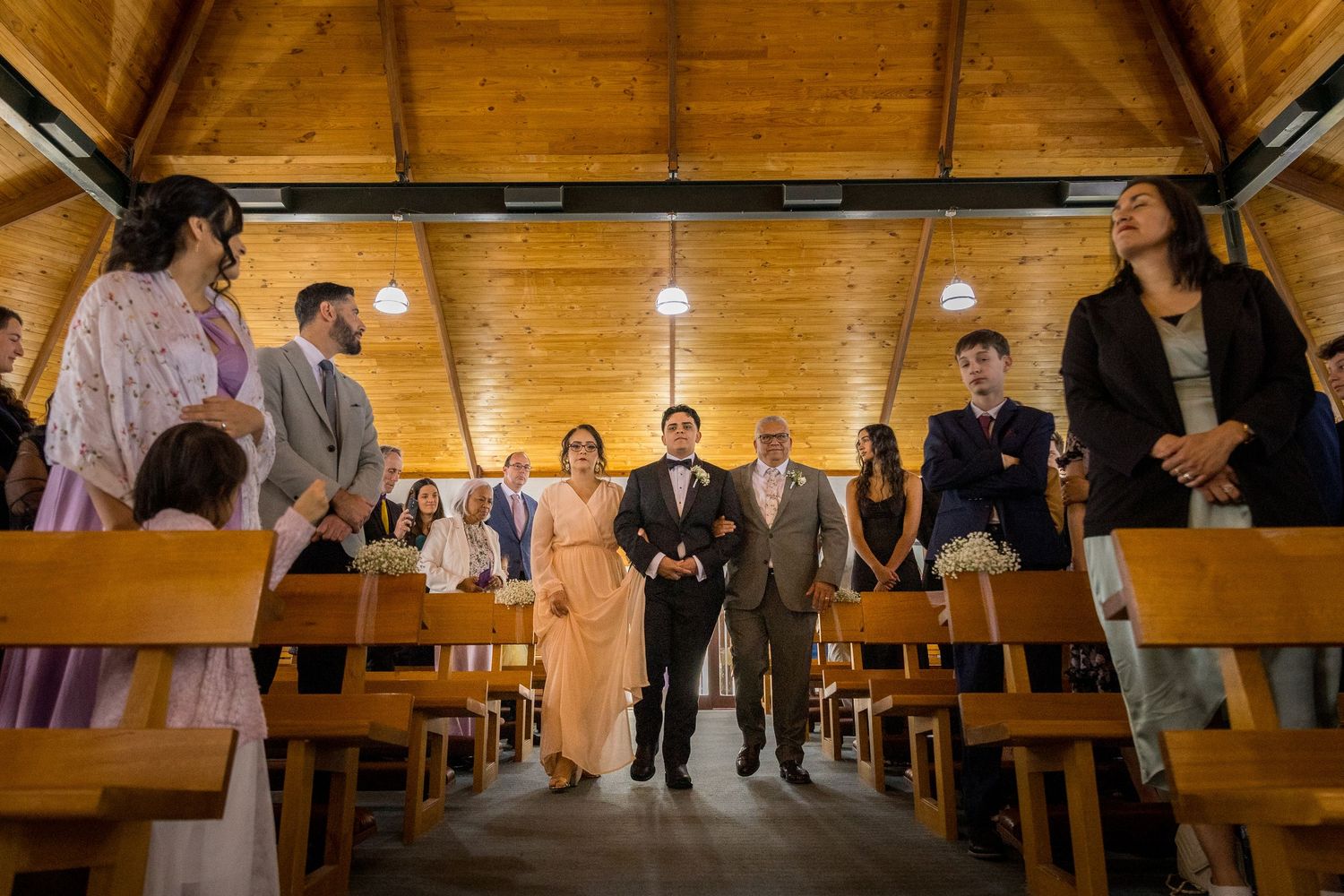 Wedding ceremony in a wooden church with guests seated in wooden pews.