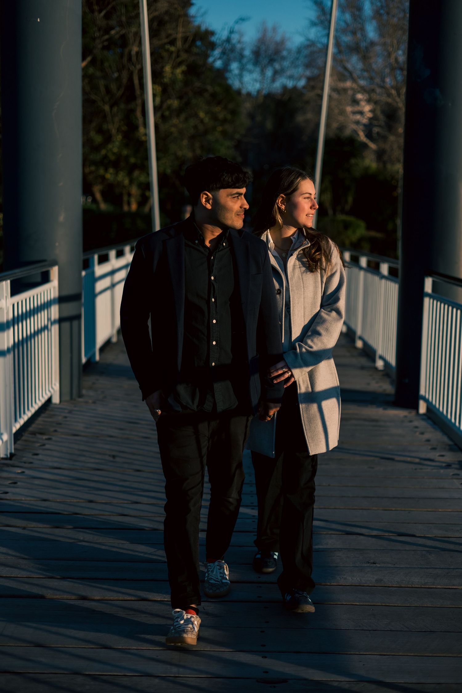 Couple walking together on a wooden boardwalk during golden hour with dramatic shadows and lighting.