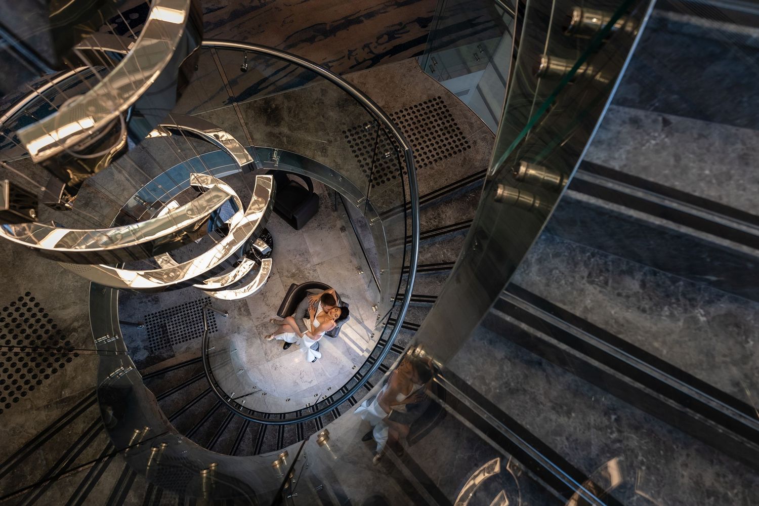 Aerial view of a couple embracing at the bottom of a stunning spiral staircase in an ornate building.