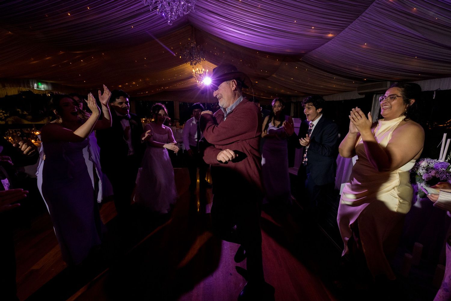 Wedding reception dance floor filled with guests under purple ambient lighting.