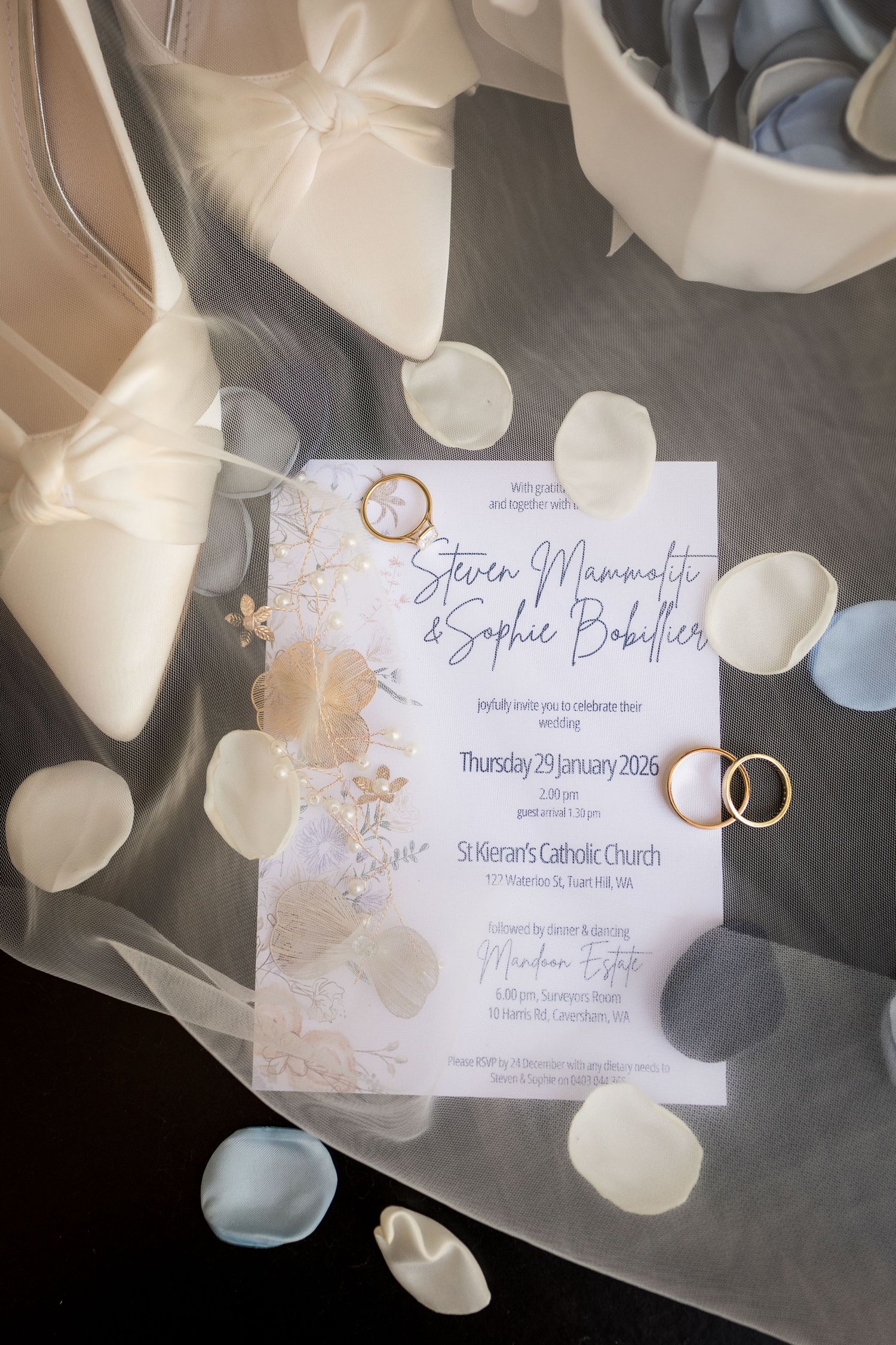 Elegant wedding invitation for Steven Mammaliti and Sophie Bobillier surrounded by rose petals and gold rings.