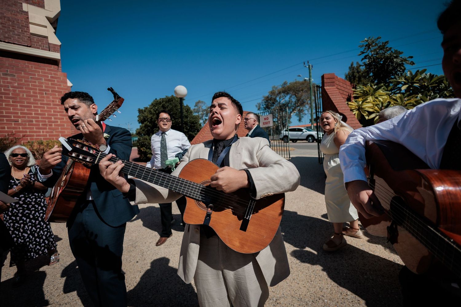 Musicians playing guitars and singing outdoors at a wedding celebration on a sunny day.