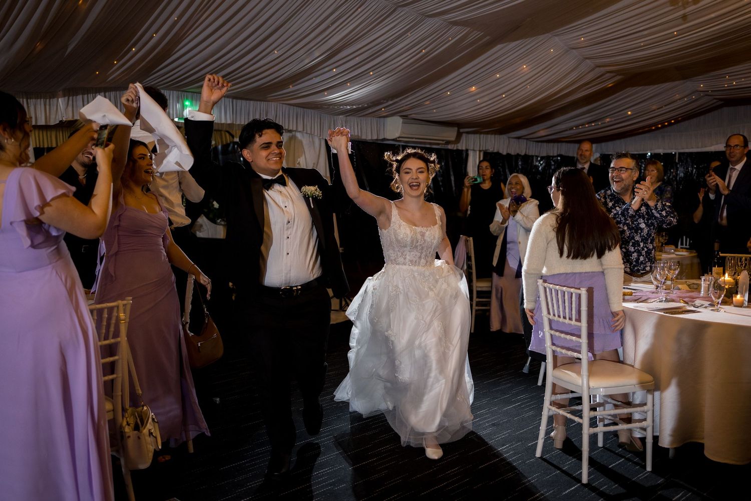Wedding reception celebration in a dimly lit venue with draped ceiling decor.