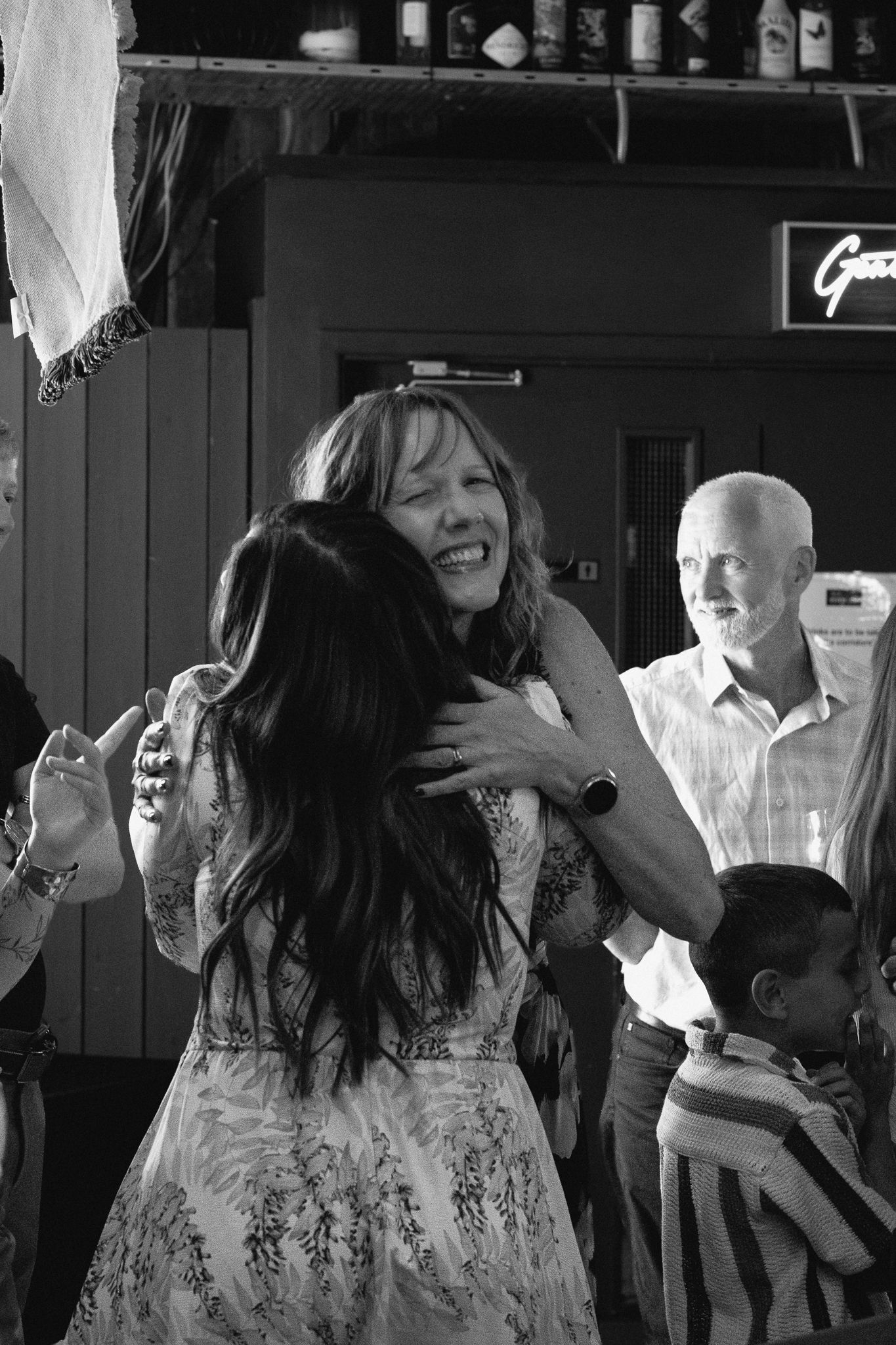 Two women sharing a warm hug at a bar gathering in black and white photo.