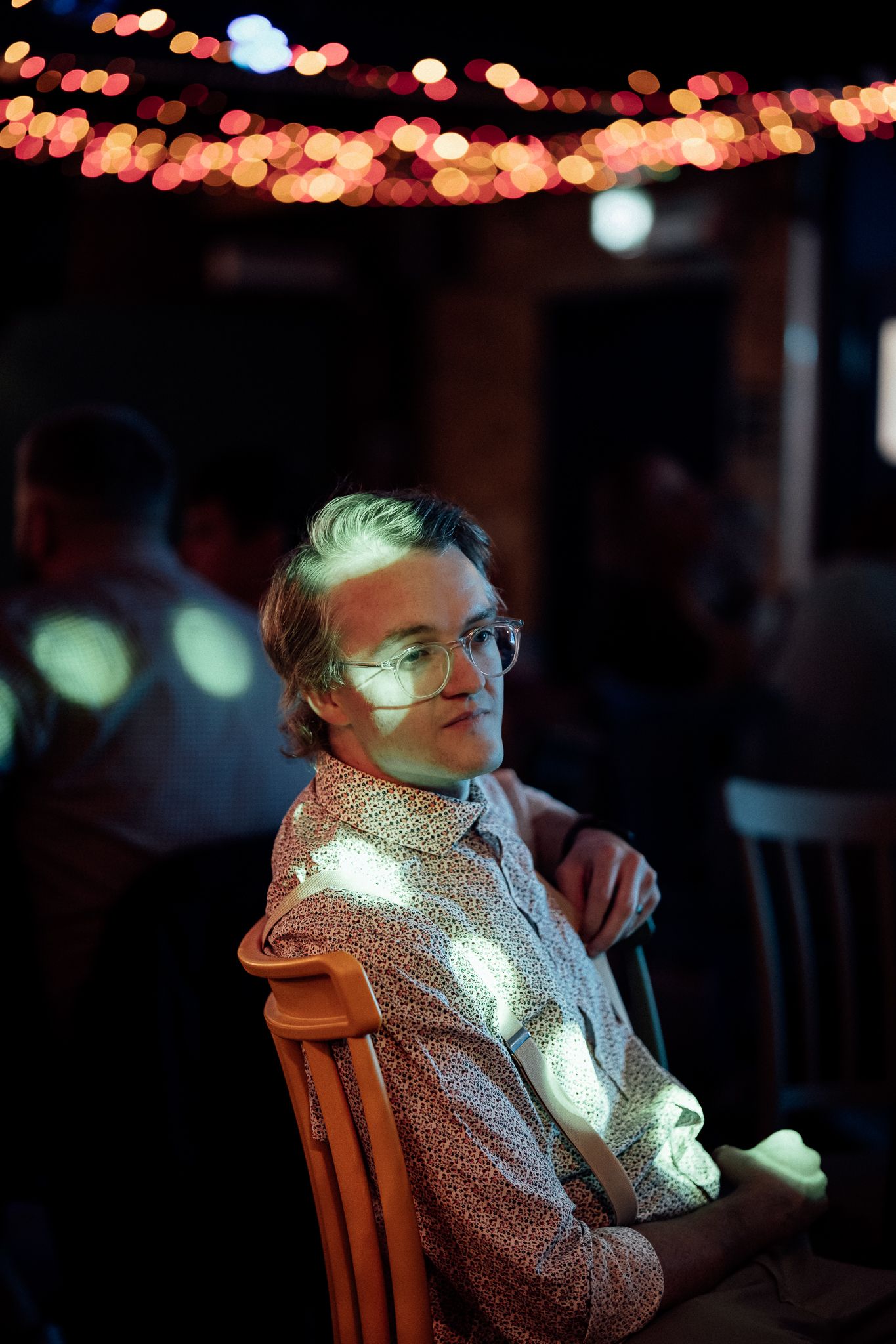Young man with glasses sitting in colorful bokeh lights at party.