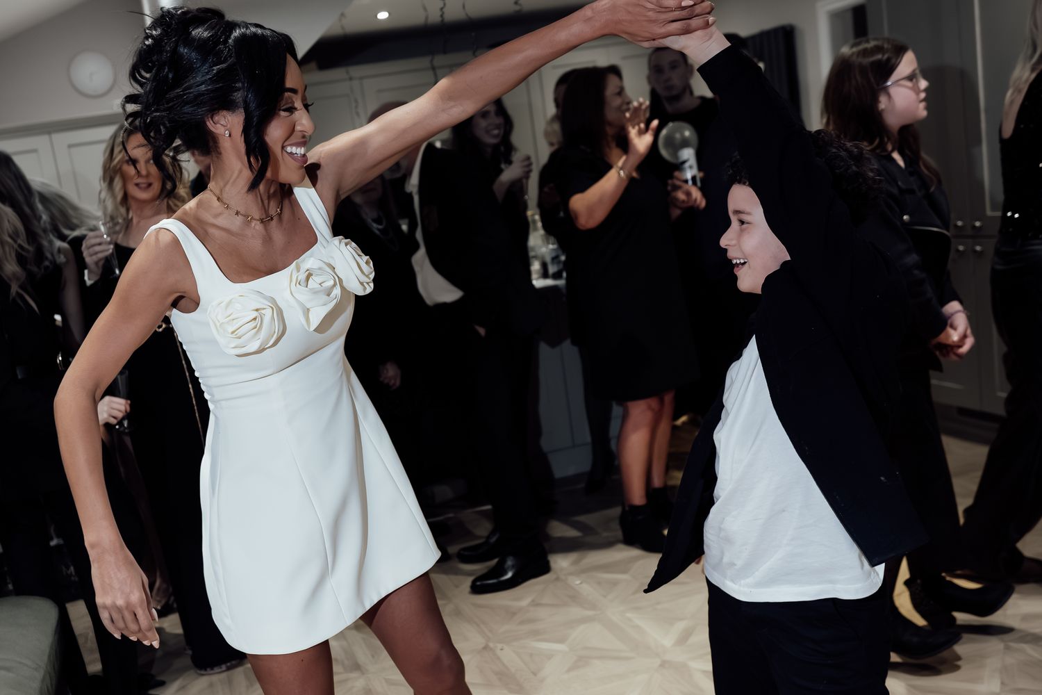 Energetic dancers in white outfits moving on a dark dance floor during a celebration.