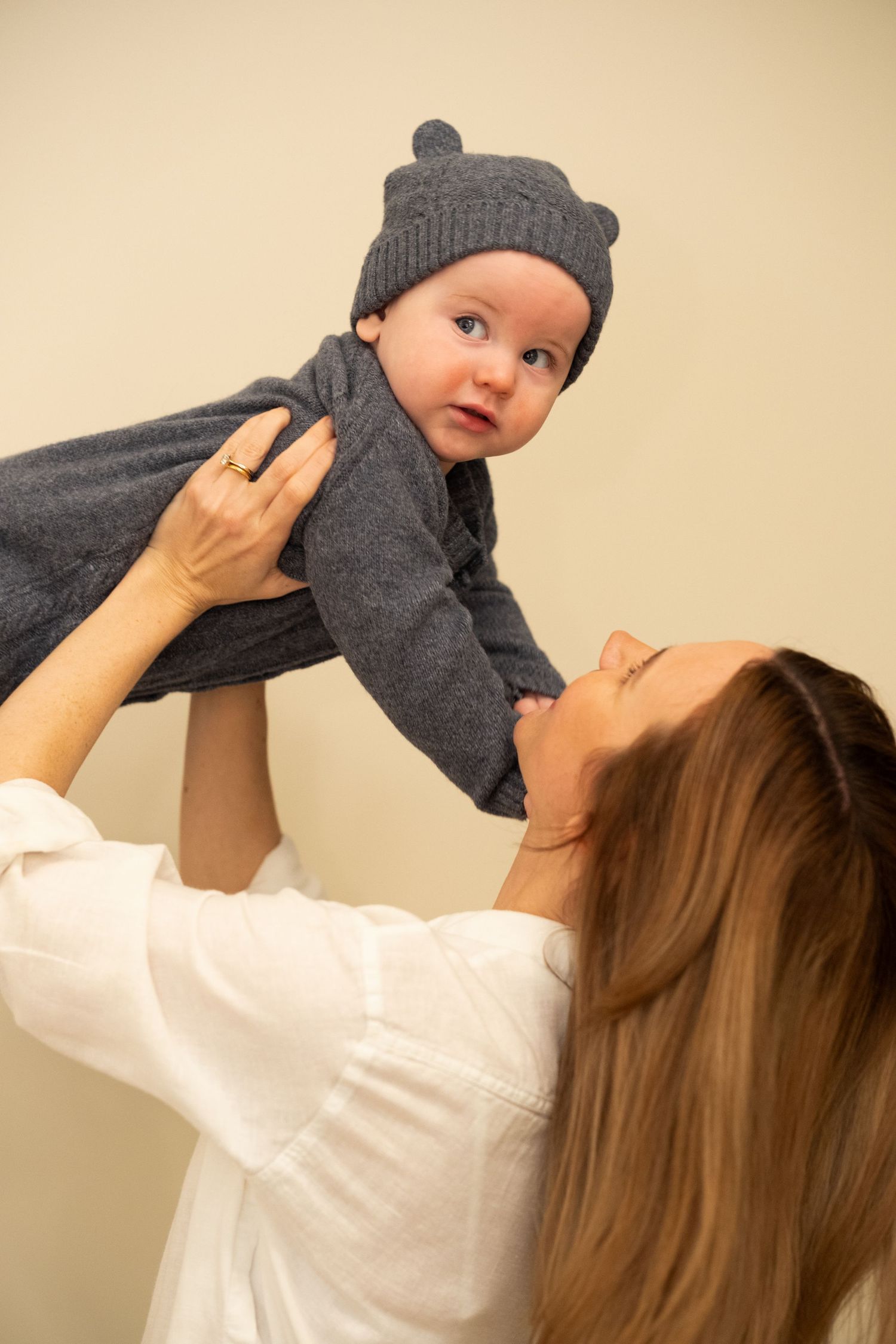 A series of photos showing someone lifting a baby wearing a gray outfit and beanie against a beige wall.