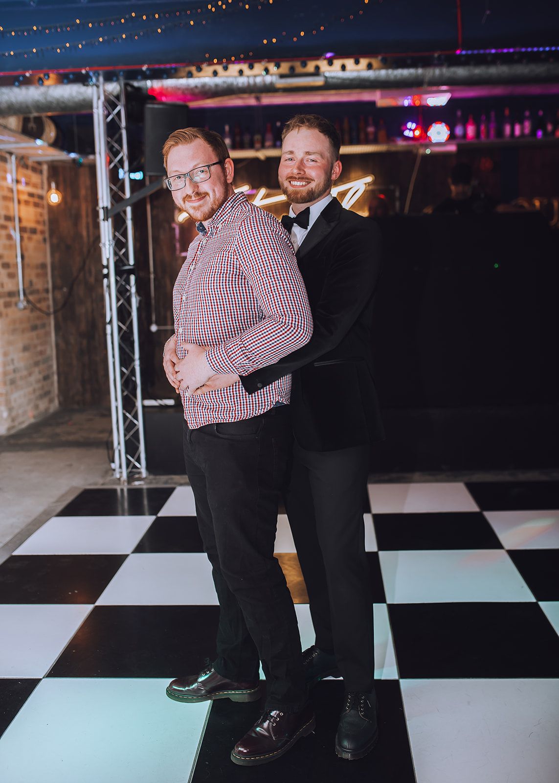 Two people dance together on a black and white checkered dance floor under venue lighting.