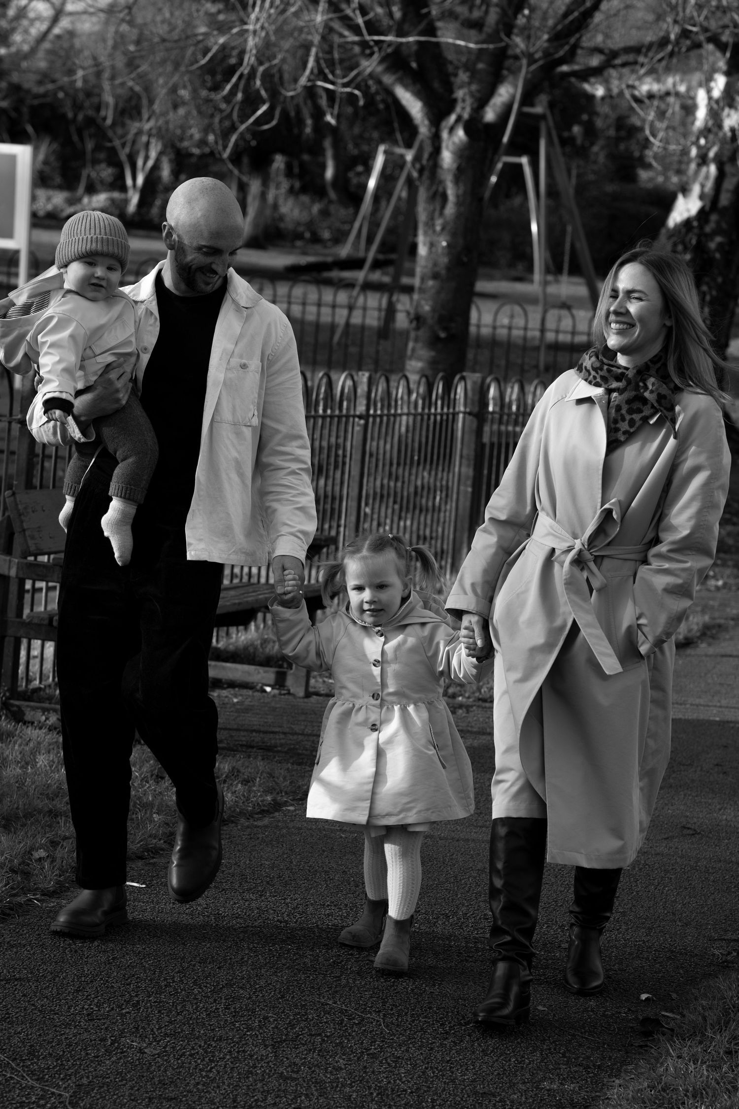 A group of people walk together in a park wearing light colored coats on an autumn day.