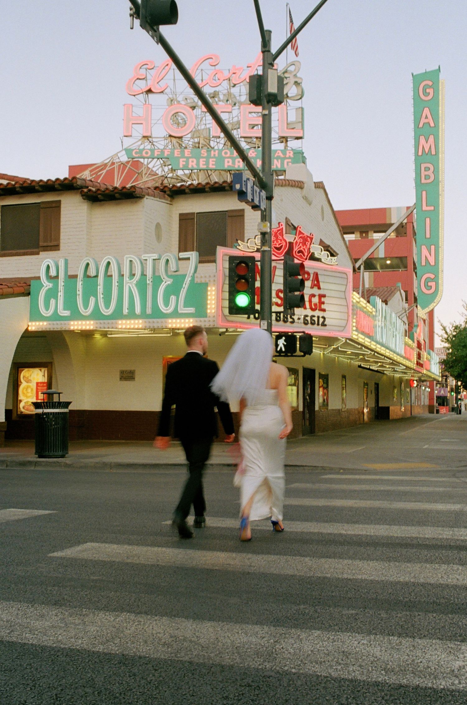 Two pedestrians cross the street in front of El Cortez casino with vintage neon signs glowing in downtown Las Vegas.