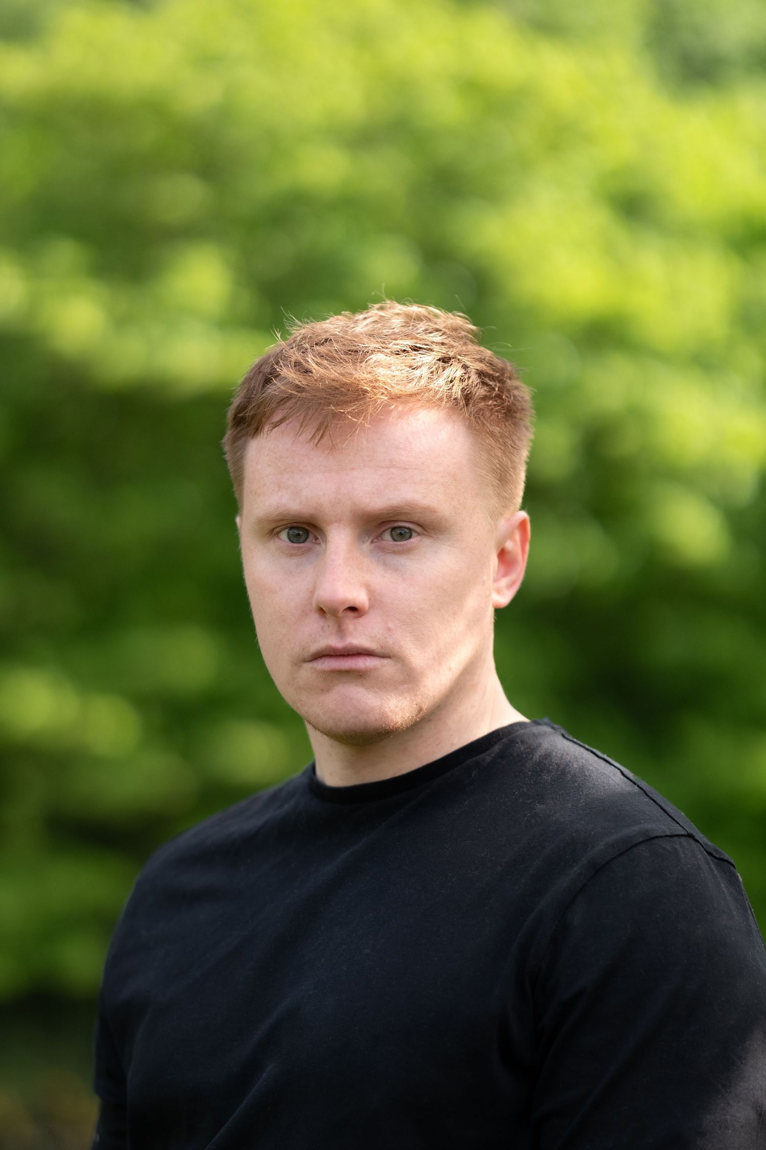 Portrait of someone wearing a black sweater against a blurred green foliage background in natural lighting.