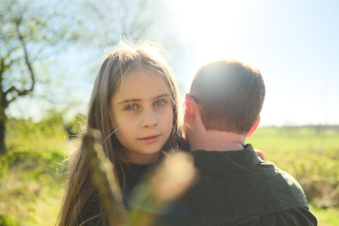 Two people share a tender moment outdoors in golden sunlight with a soft blurred background.