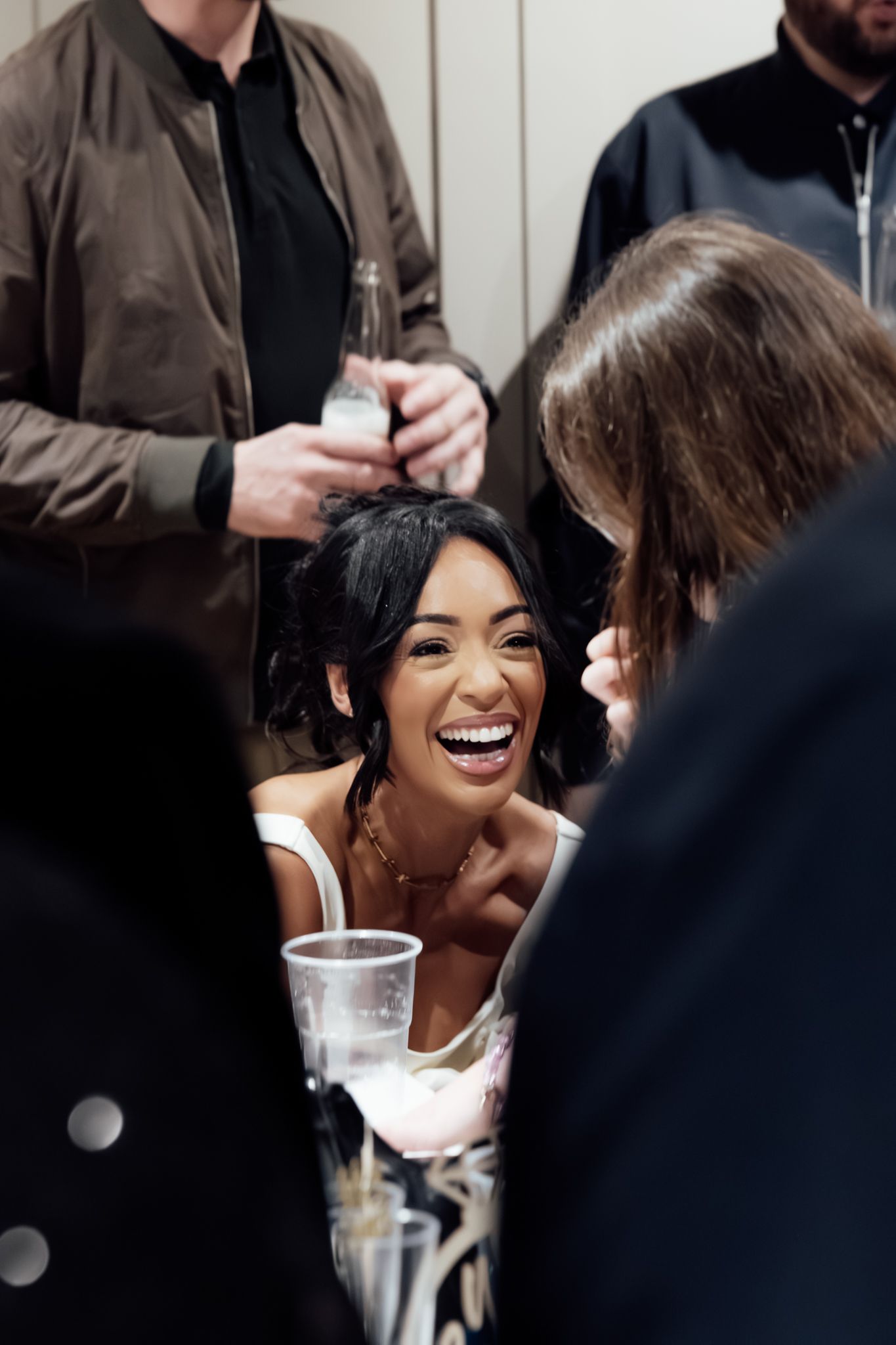 A candid moment of laughter during a wedding reception as guests gather around drinks.
