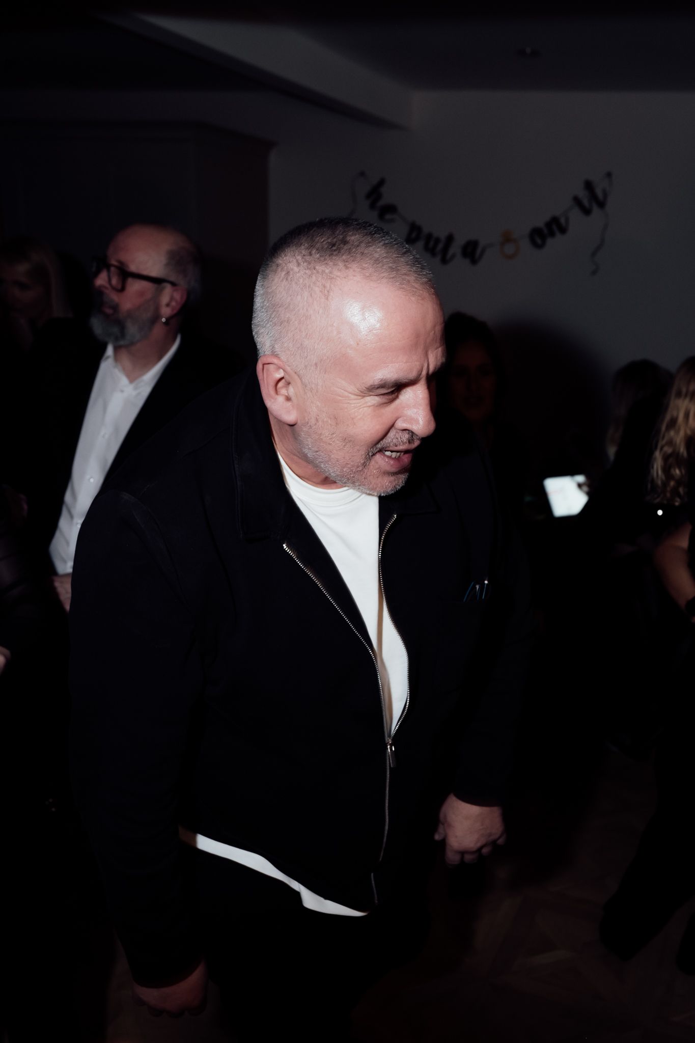 A guest in a black jacket and white shirt attending an evening event.