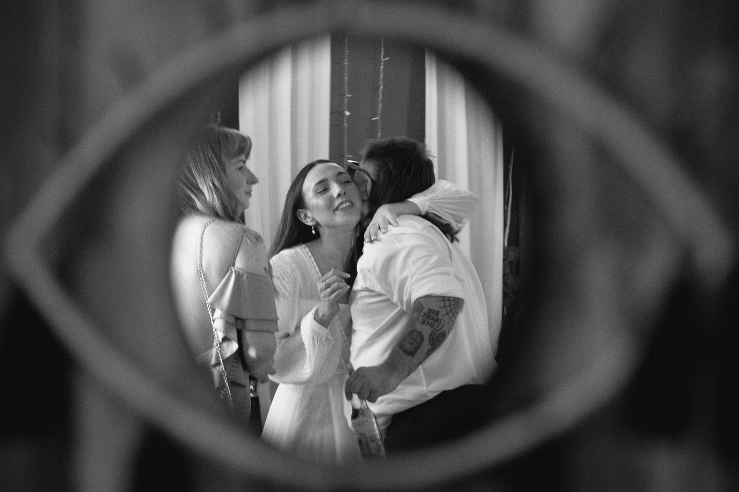 Black and white photo of a couple sharing a tender moment viewed through a decorative eye-shaped mirror frame.