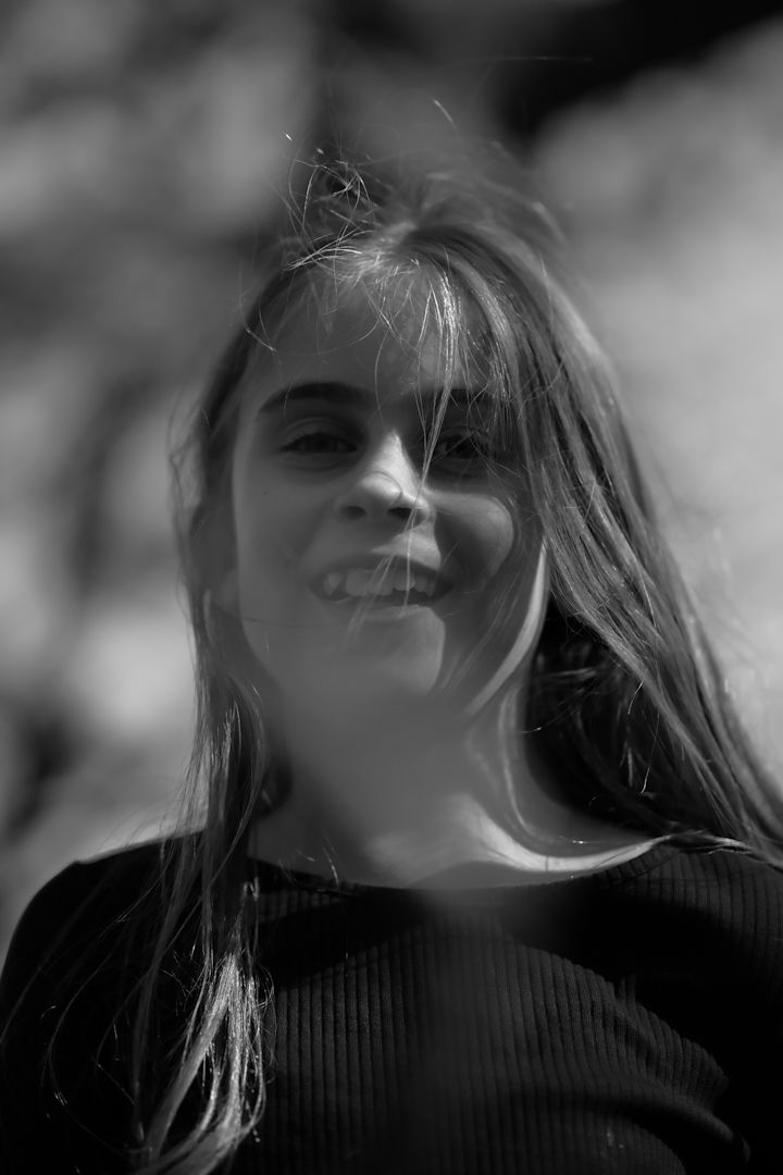 Black and white portrait of a smiling young girl with long hair outdoors.