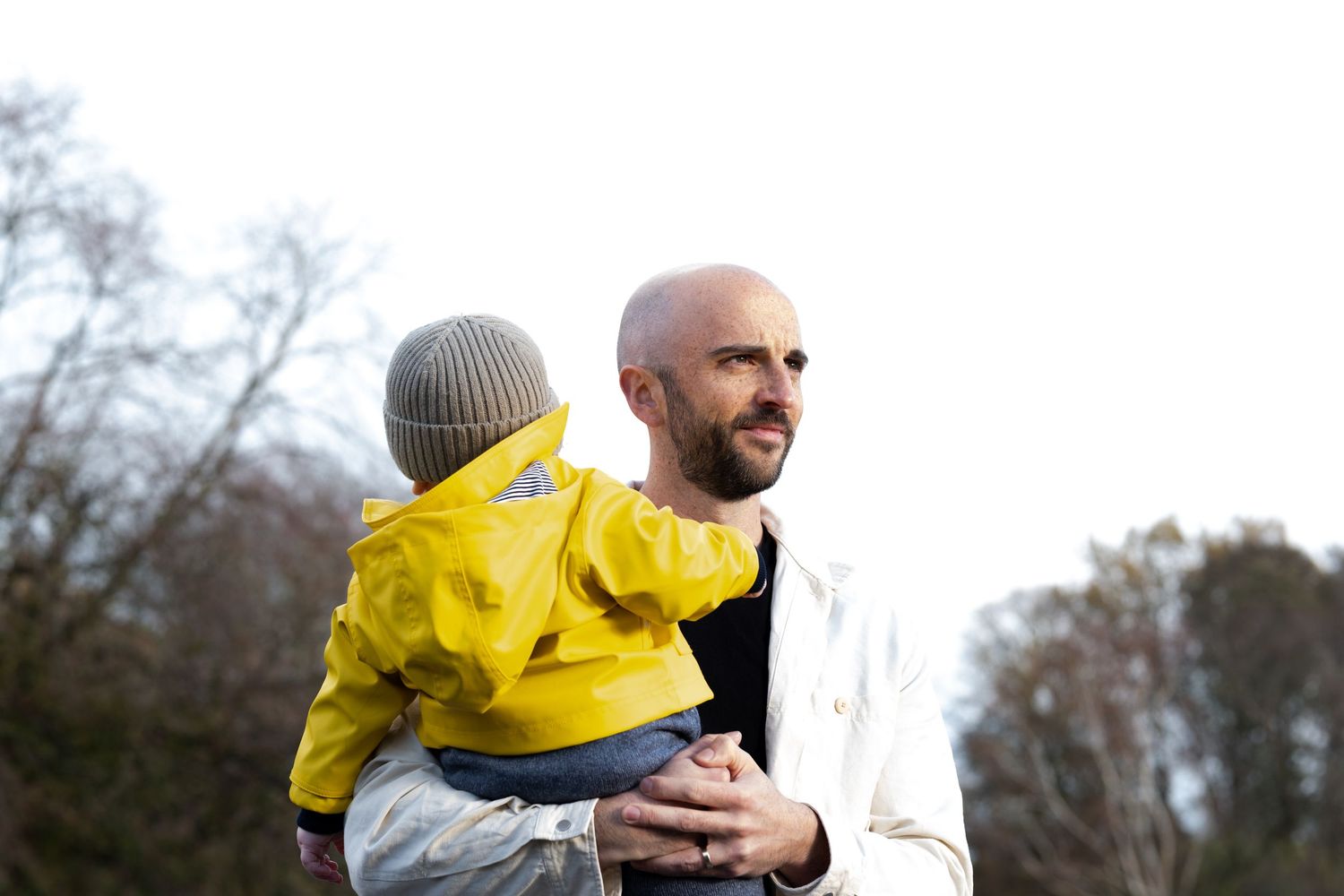 Parent and child wearing winter coats share a tender moment outdoors on a cloudy day.
