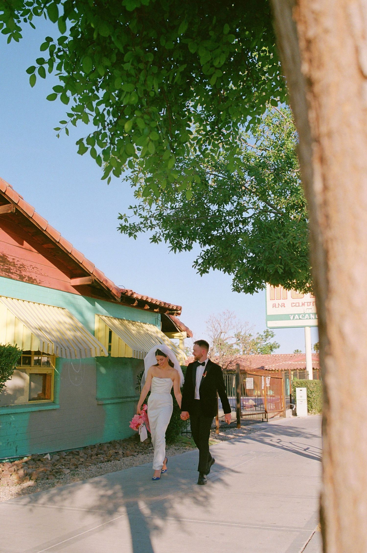 A panoramic view of people walking outside adobe-style buildings with turquoise trim under a bright blue sky.