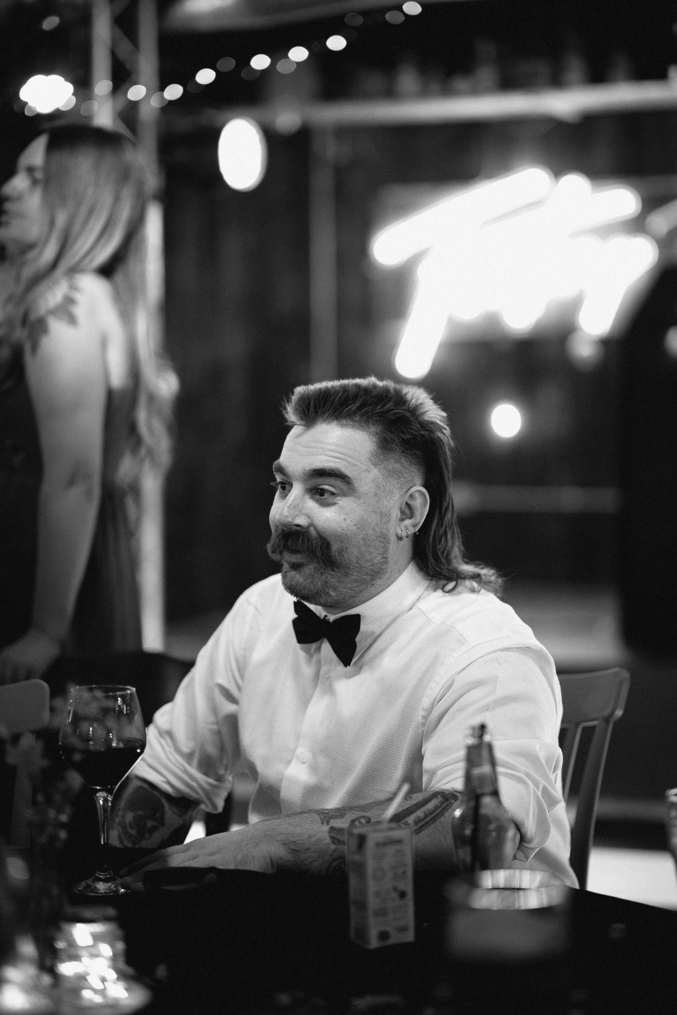 Man with mustache and bow tie smiling at wedding reception table.