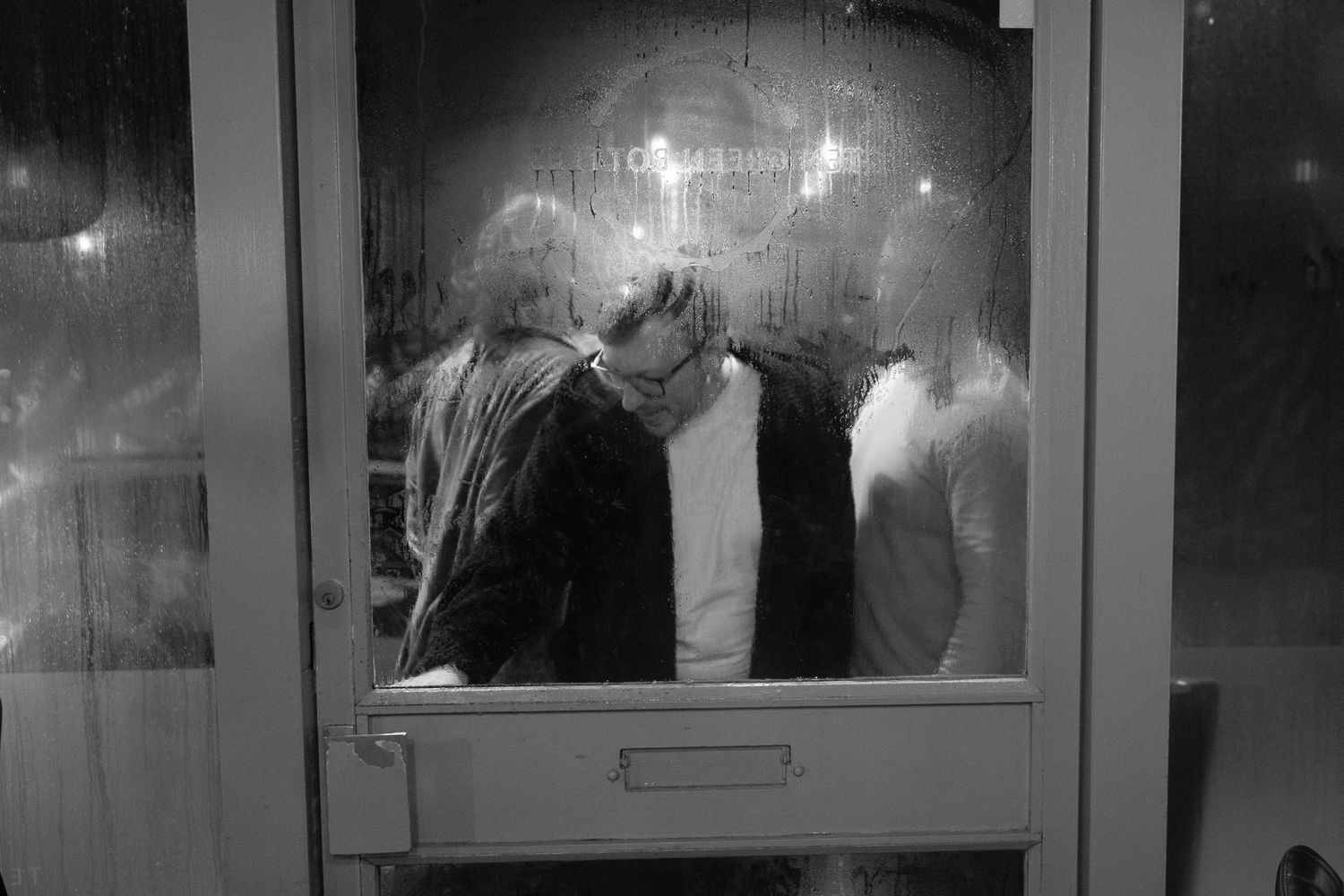 A black and white photo shows a row of illuminated glass display cases in what appears to be a museum or gallery setting.