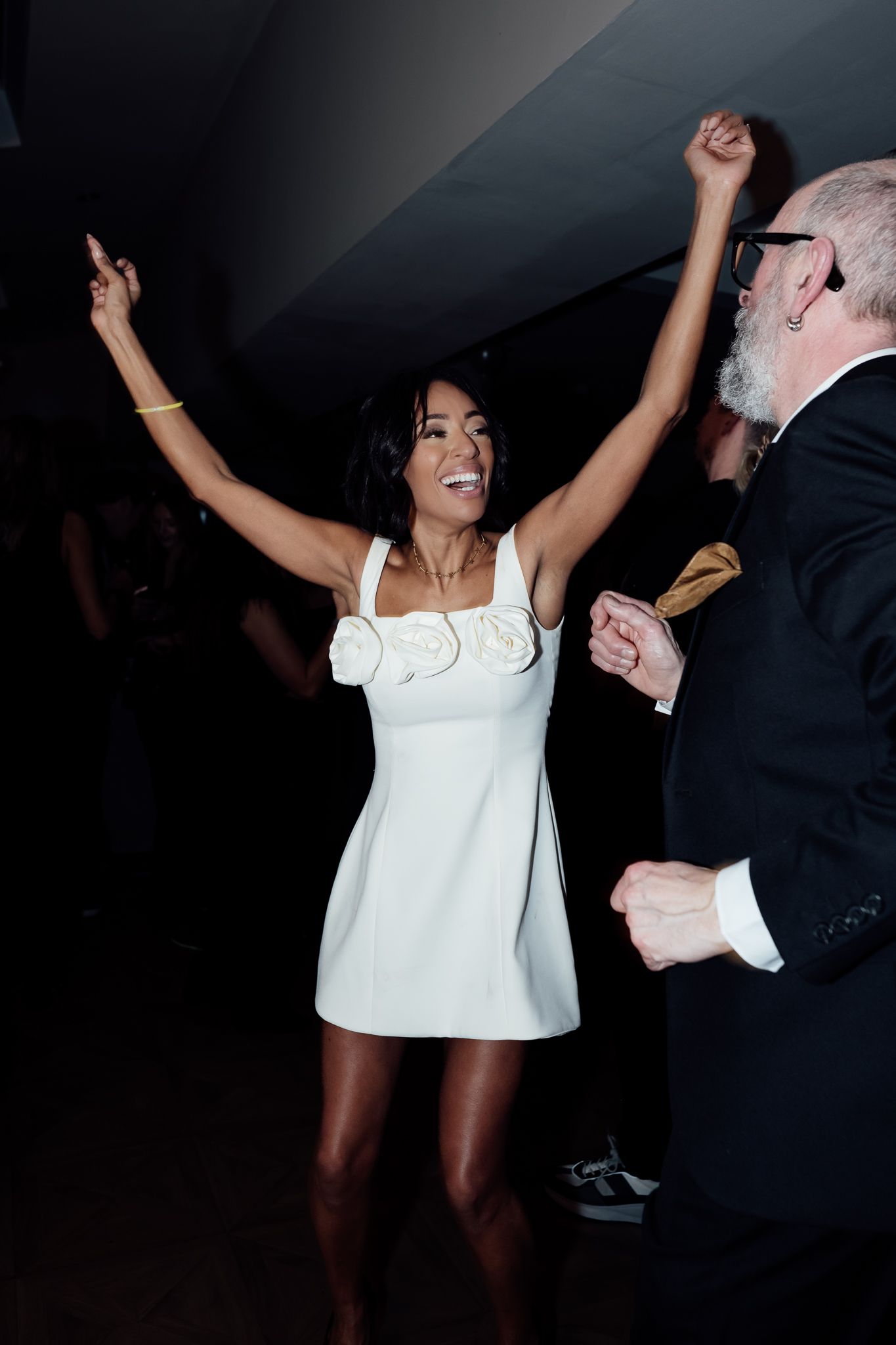 Partygoers dancing enthusiastically in a dark room with one person wearing a white top.