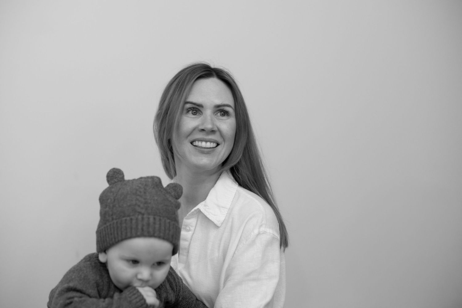 A parent and baby in a knit hat share a tender moment in black and white photography.