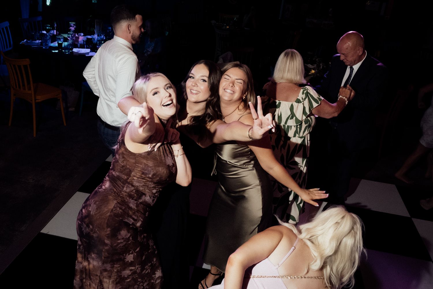 Women in elegant dresses posing and smiling together on a dance floor at a formal evening event.