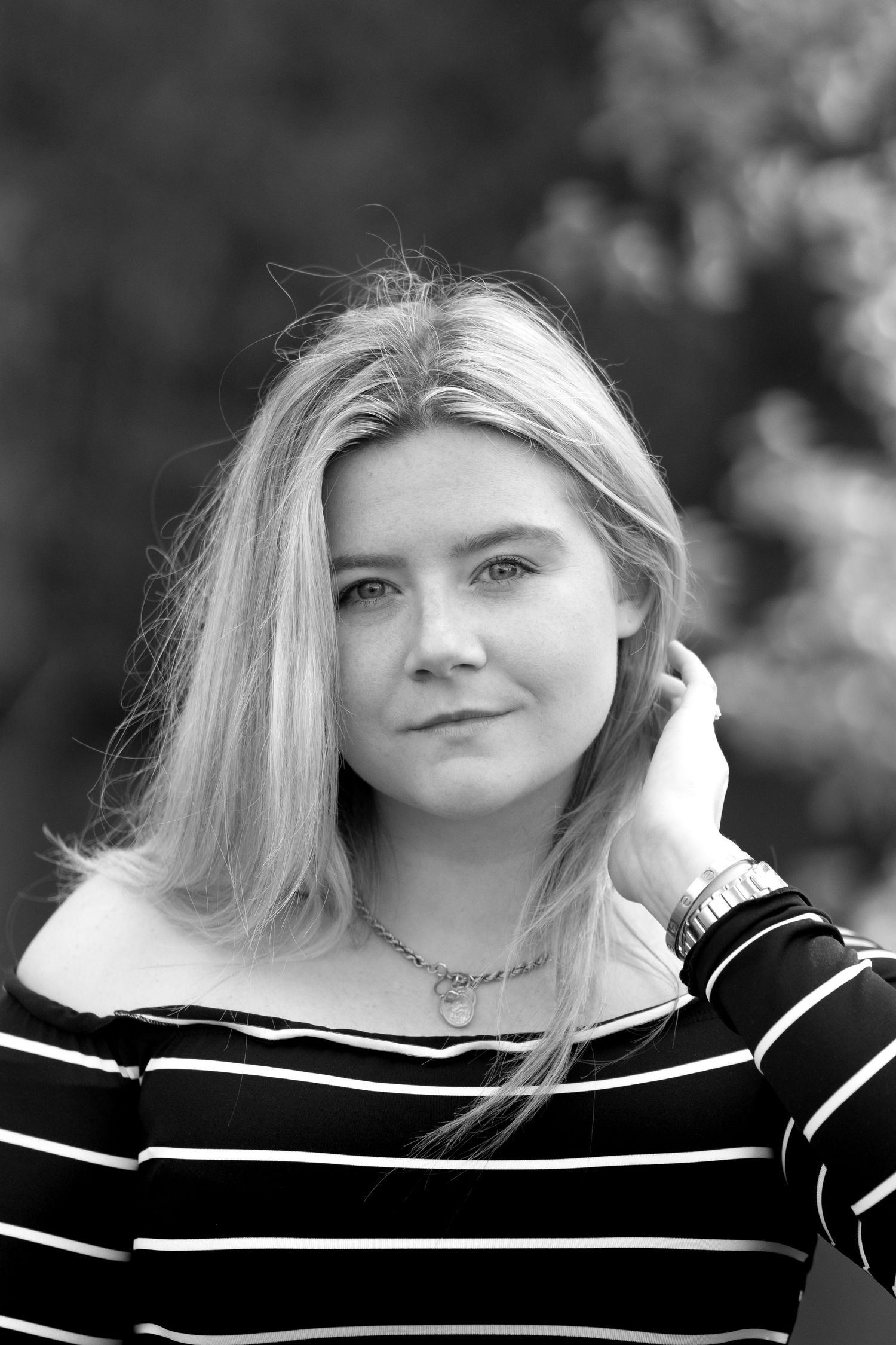 A person wearing a black and white striped sweater poses against a blurred outdoor background.