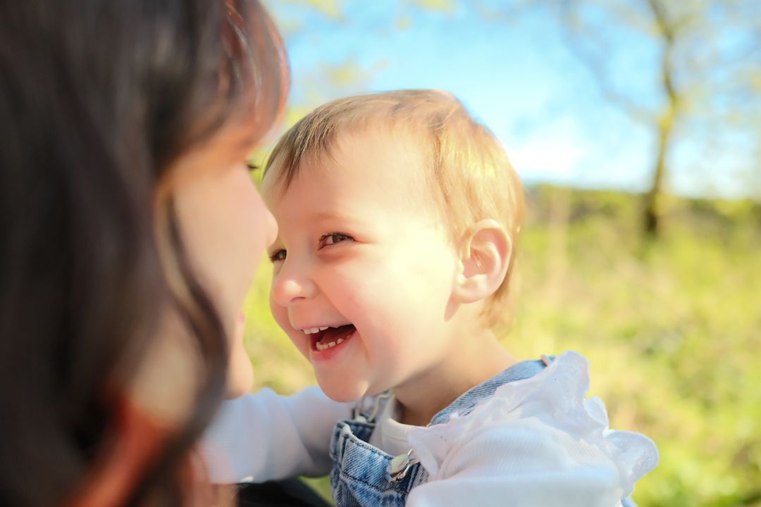A baby laughs and plays outdoors in a sunny field with yellow wildflowers on a bright summer day.