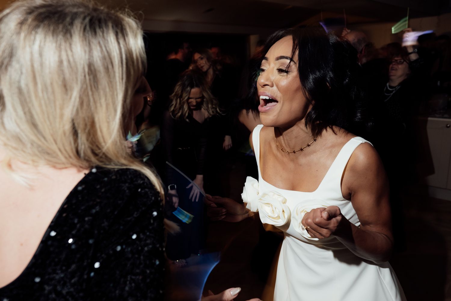 People dancing and celebrating at a lively wedding reception party on a dark dance floor.