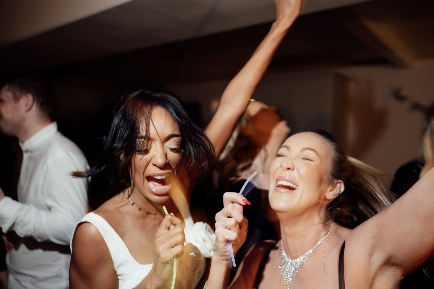 Two women singing and dancing joyfully at a wedding reception party.