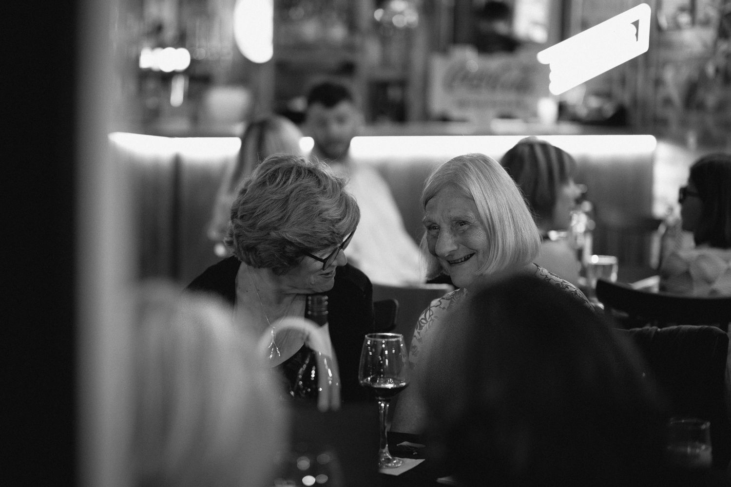Two older women laughing and chatting over wine at wedding reception.