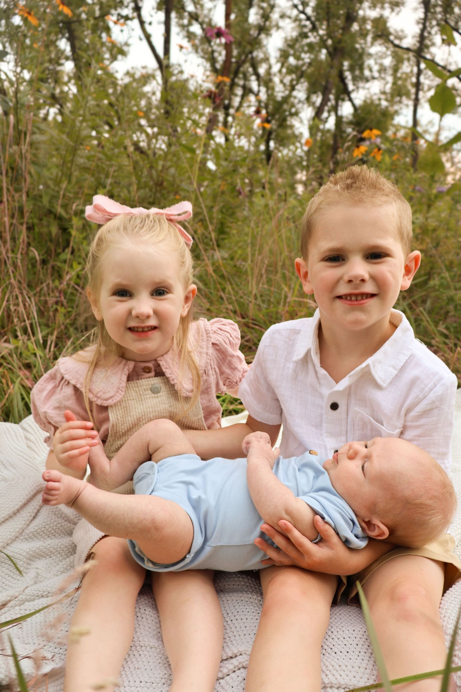 A playful sequence of children sitting together on a blanket outdoors with a baby.
