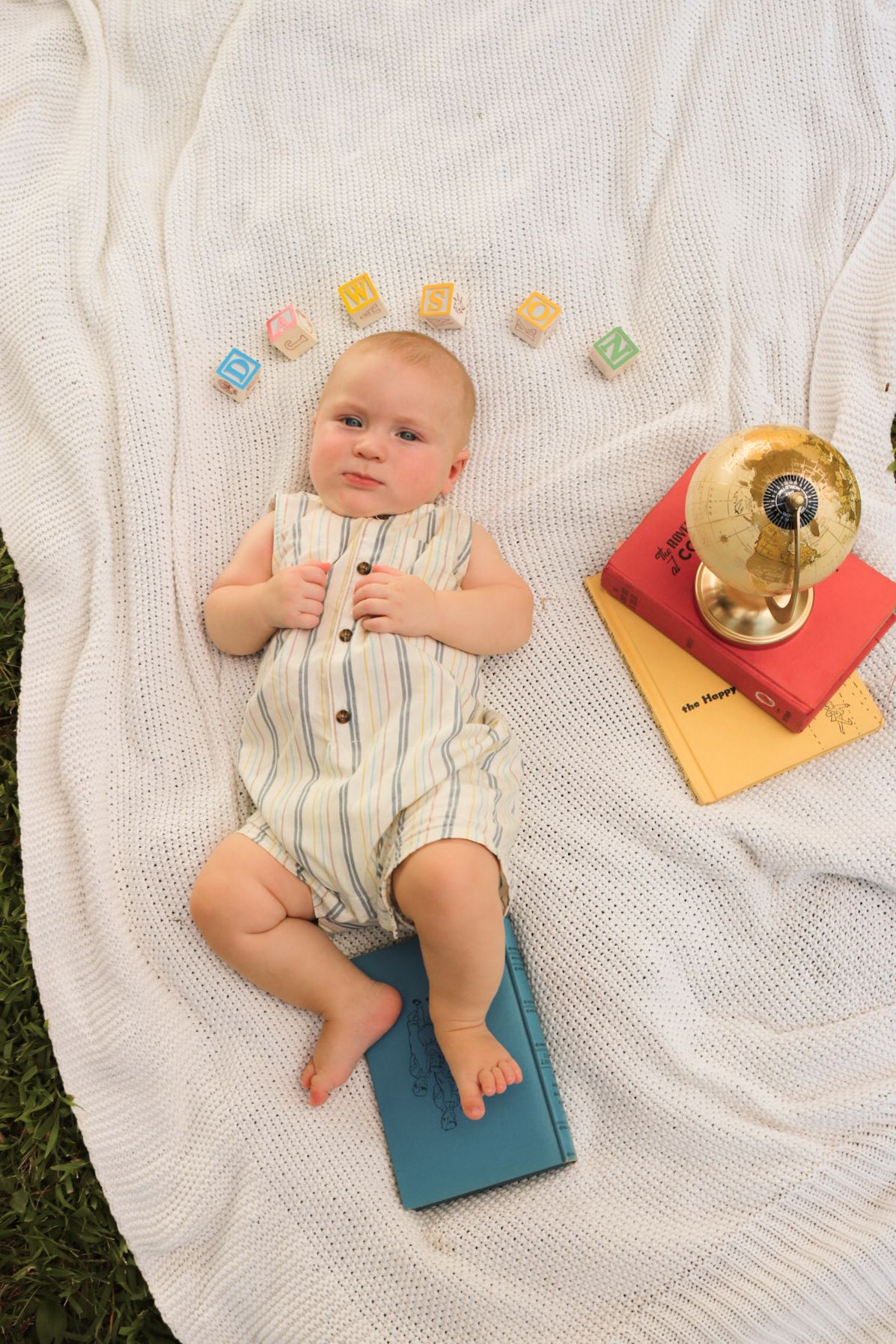 Baby lying on white knit blanket with colorful books arranged nearby.