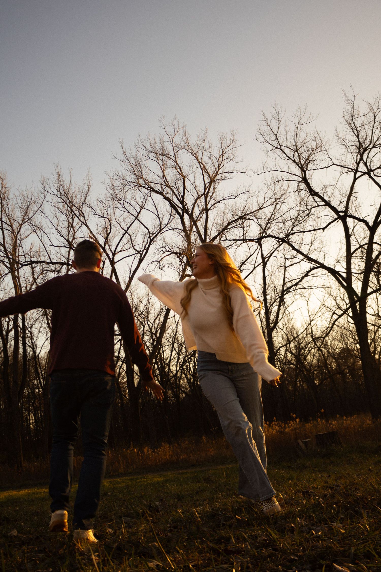 A couple dances together at sunset in a field with bare winter trees silhouetted against the dusky sky.