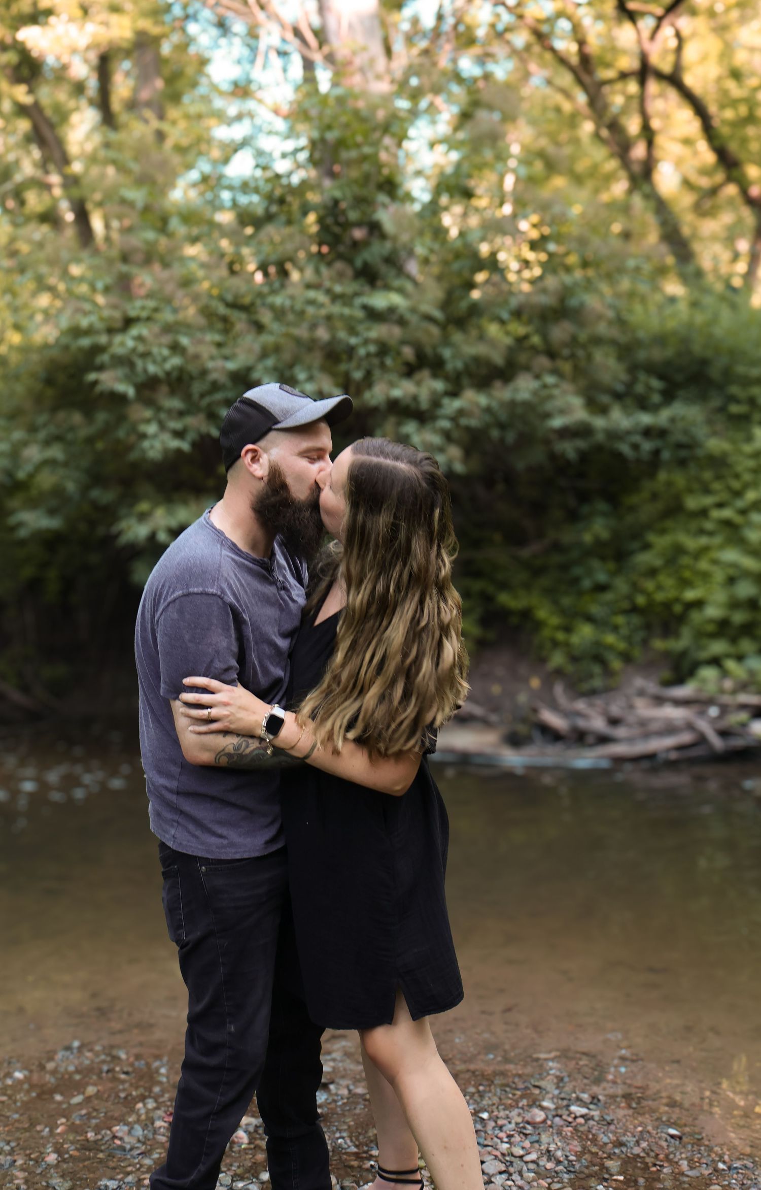 Romantic couple moment captured by creek in wooded setting.