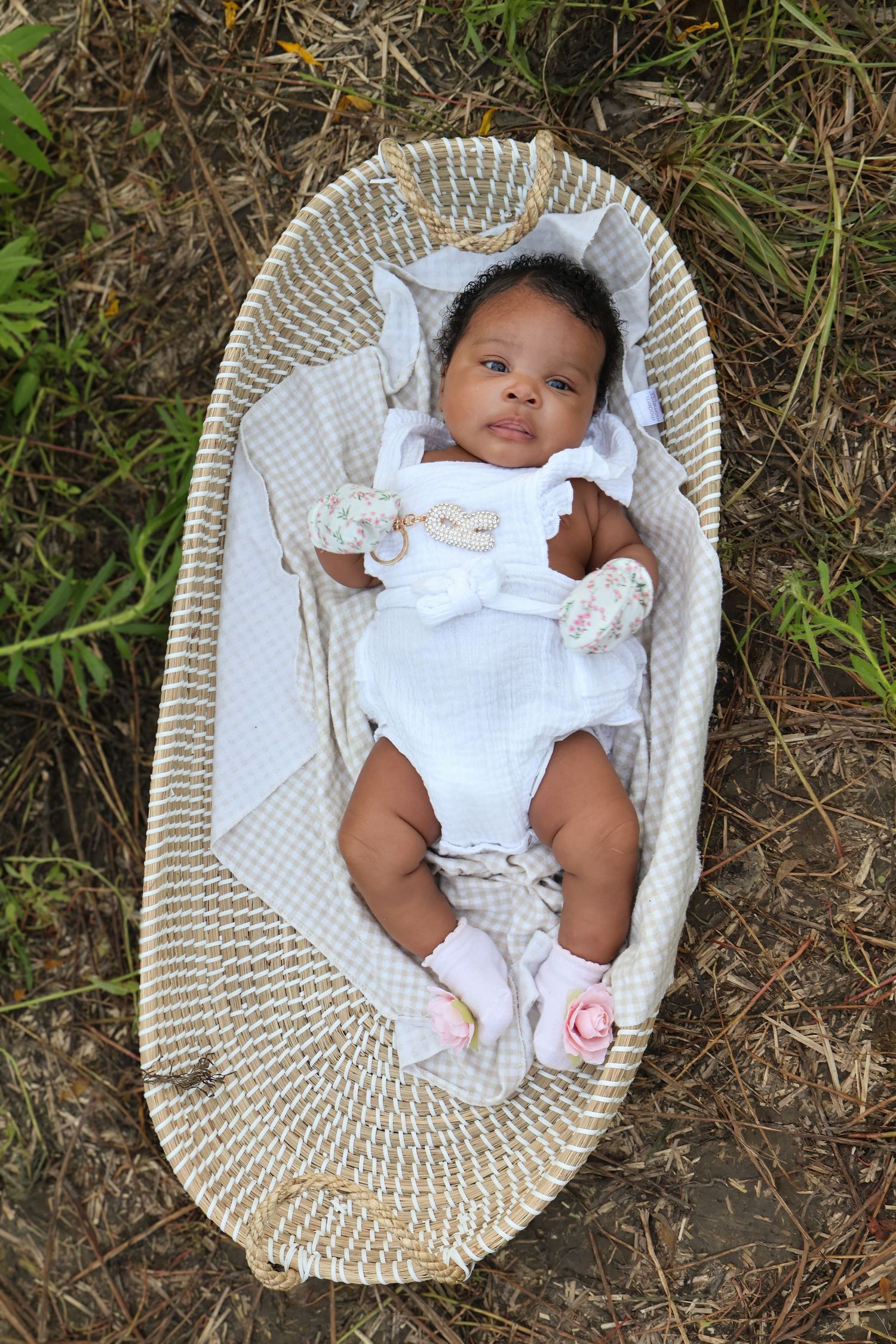 Baby resting in woven basket outdoors wearing white outfit.
