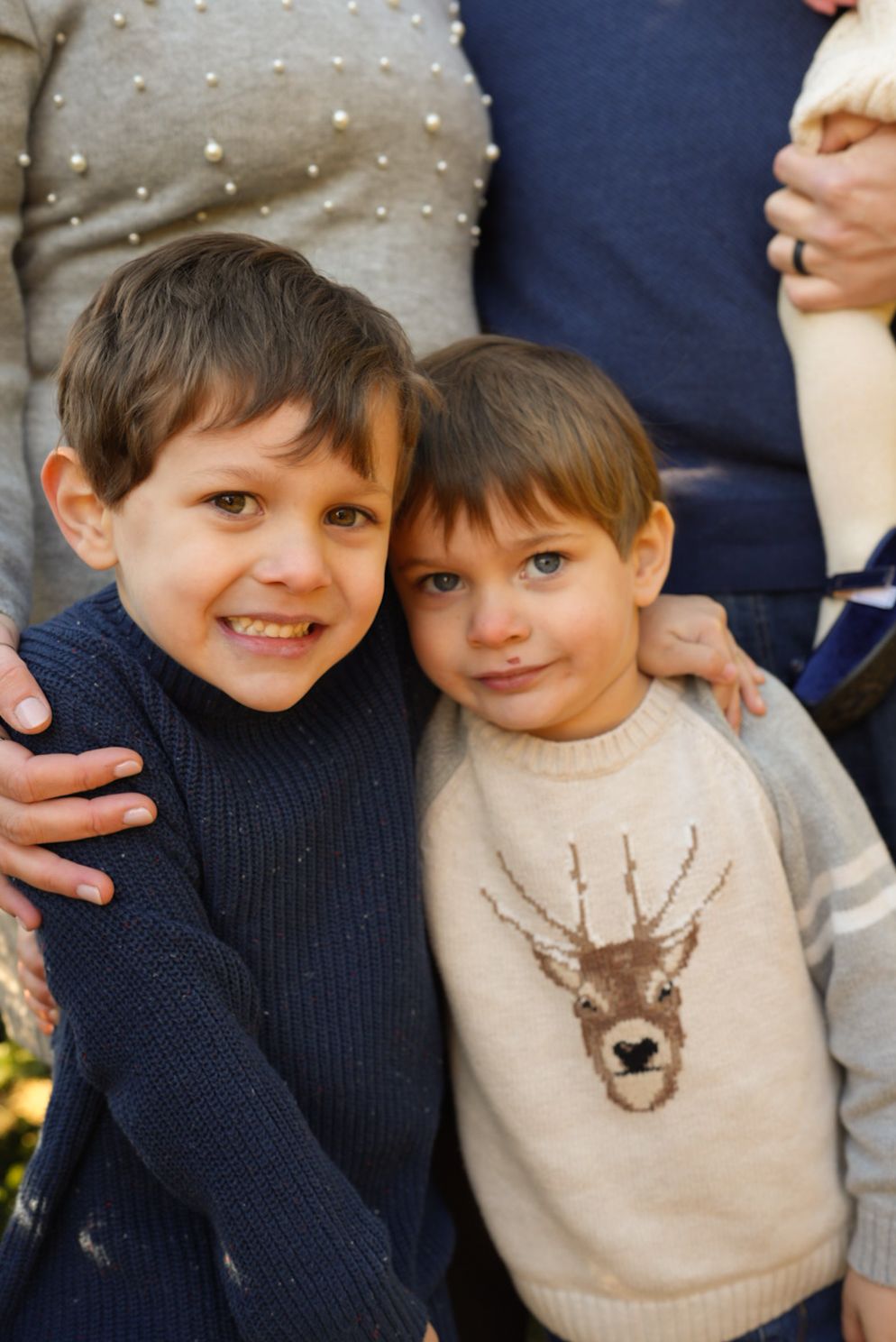 Two young children in sweaters smile together in a series of four similar photos.