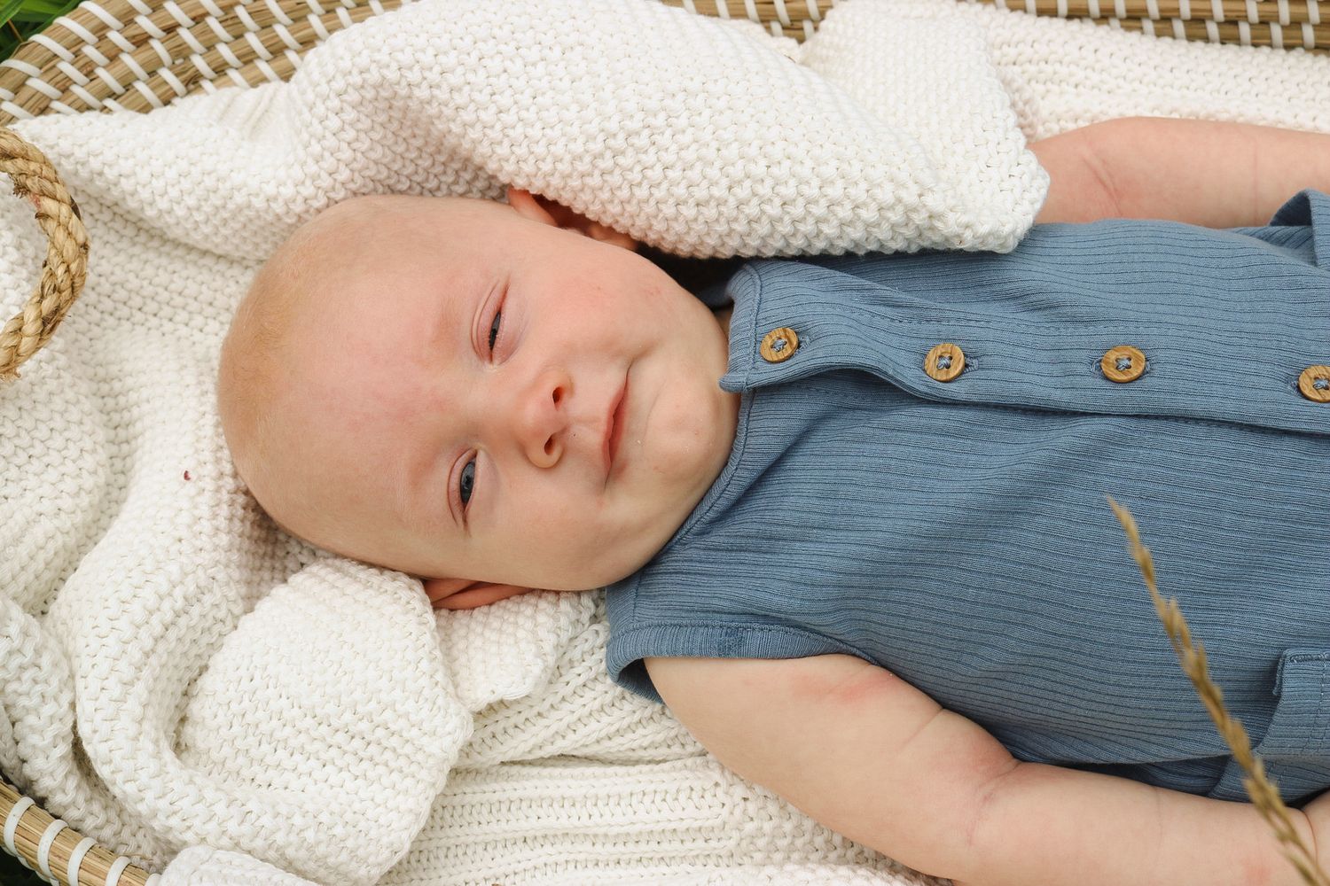 Baby sleeping peacefully on white knit blanket wearing blue outfit.
