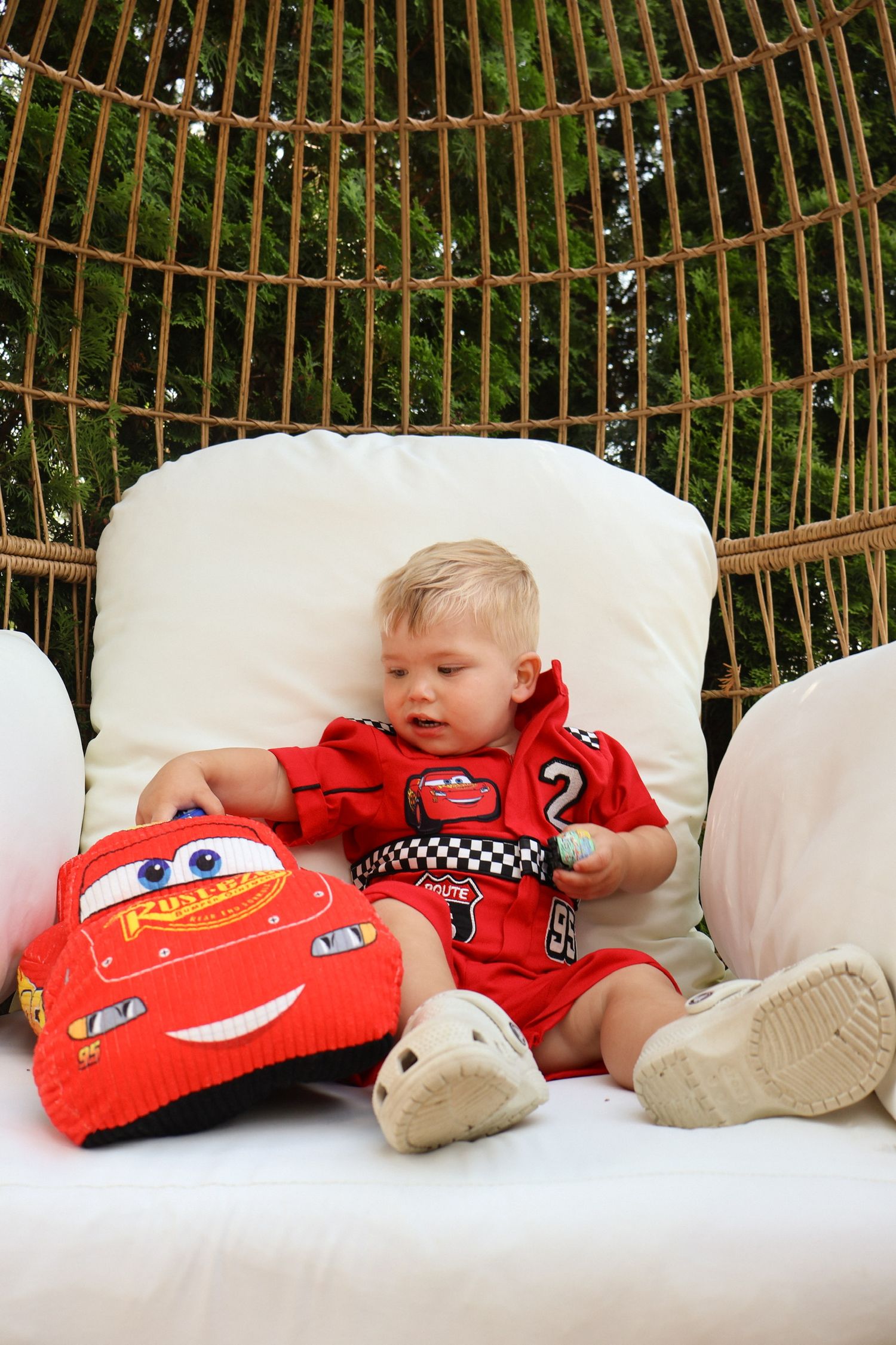 Child resting on white cushions with red Cars-themed plush toys.