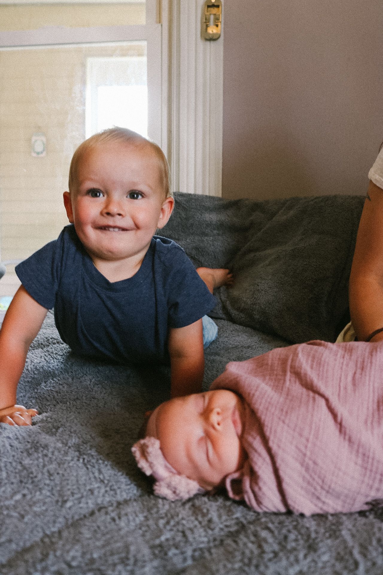 Two young children lying on a gray couch, one in a navy shirt and one in pink.