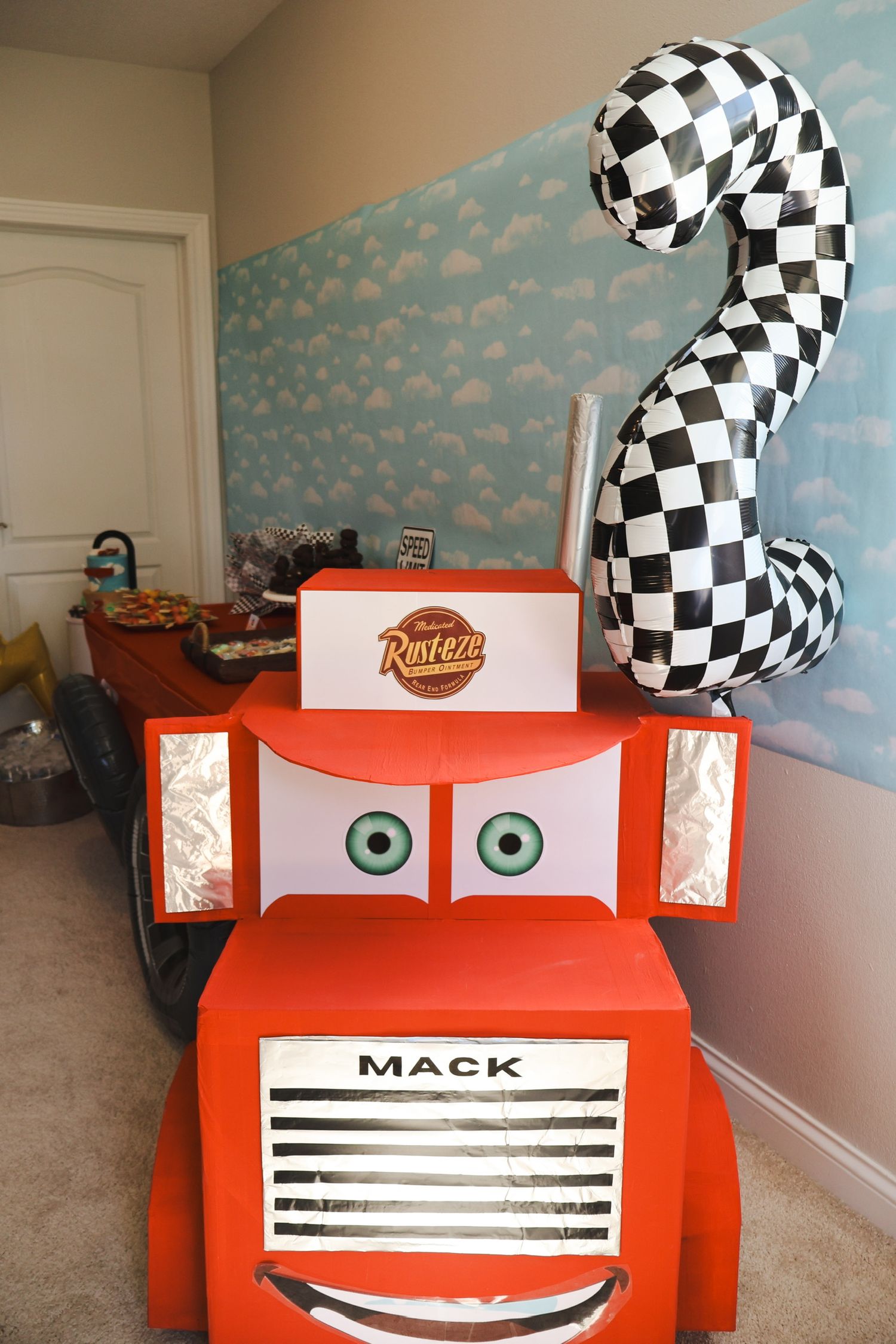 Cars-themed party decoration featuring red truck character with checkered flag on blue wall.