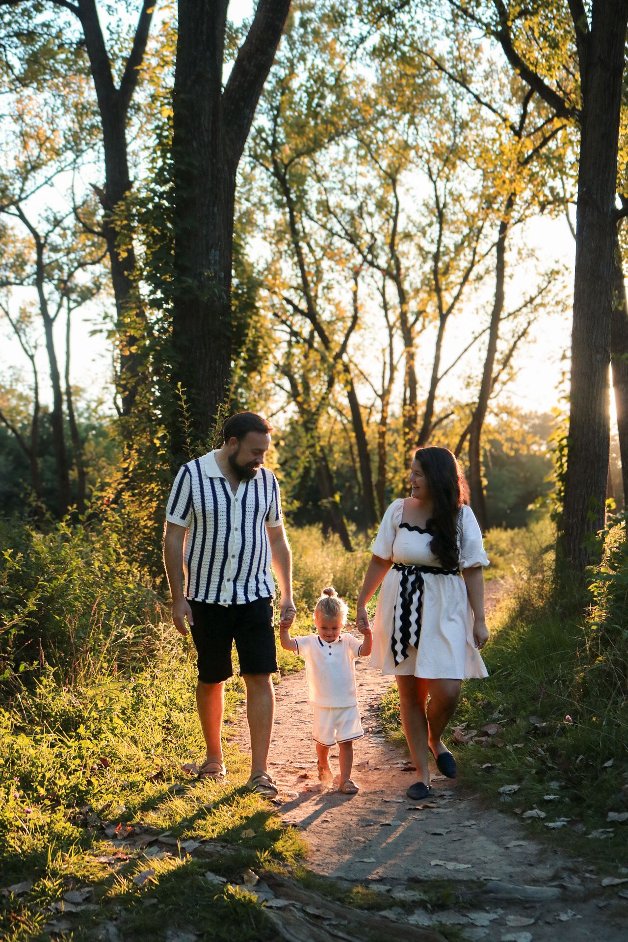 Family walking along a sunlit forest path in black and white striped outfits.