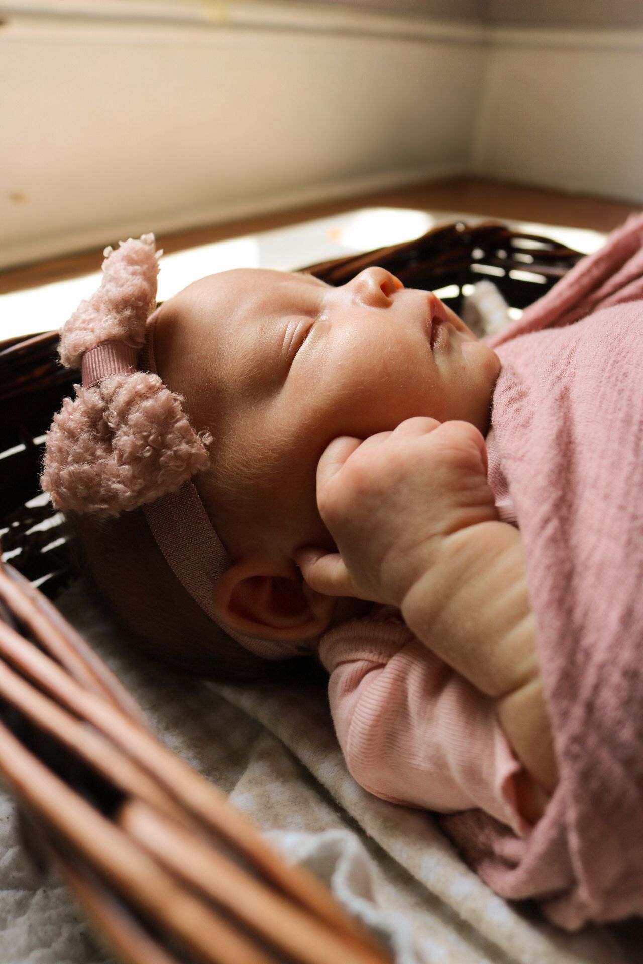 Sleeping newborn baby wrapped in soft pink blanket lying in woven basket.