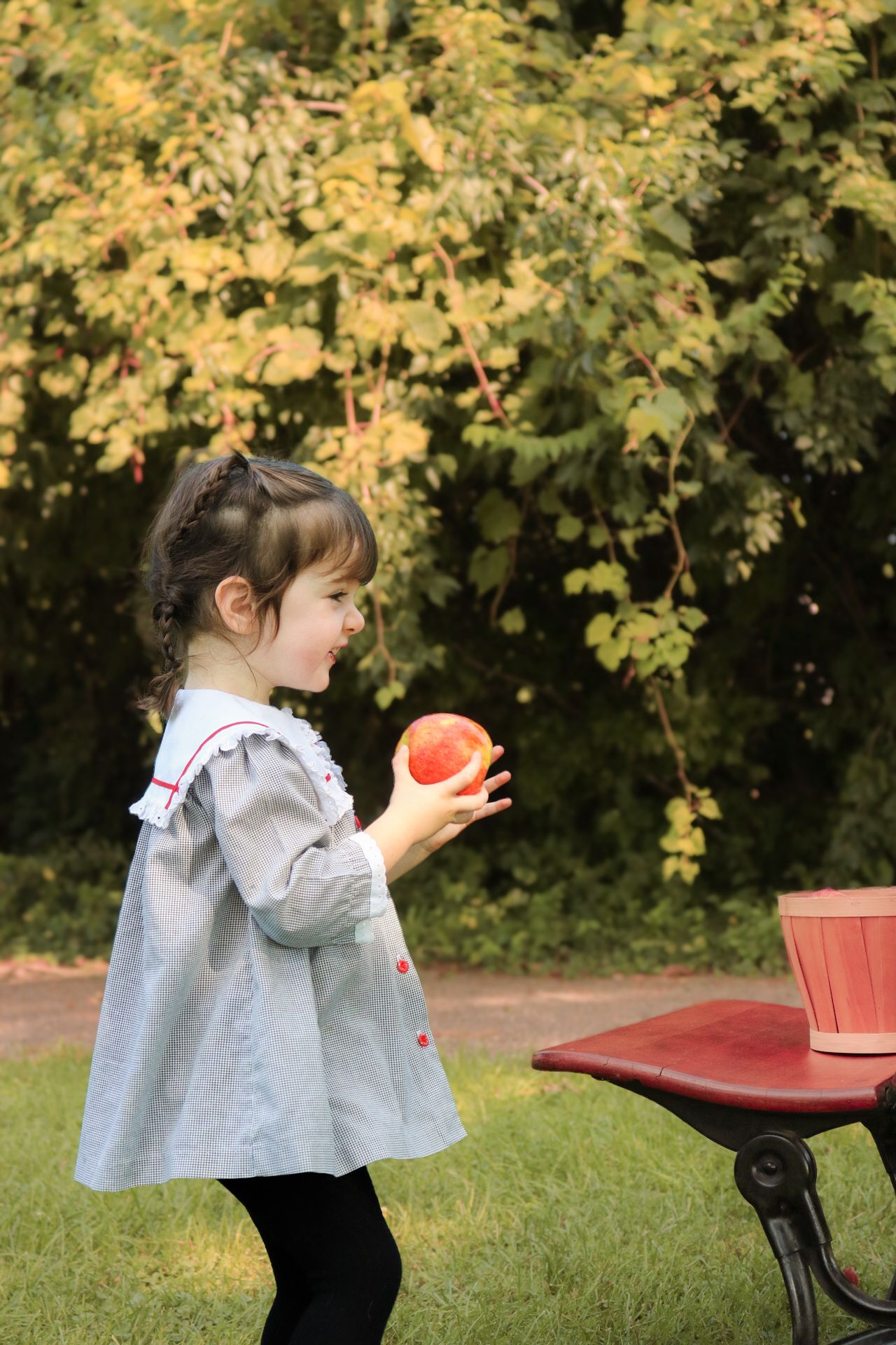 Small child in gray dress holding orange ball in garden setting.
